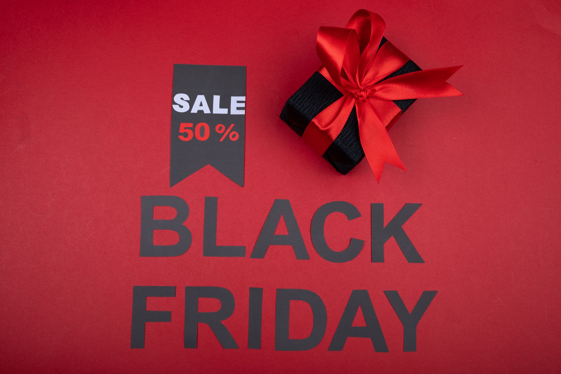 Black Friday sale banner with 50% off tag and gift box wrapped with red ribbon on red background.