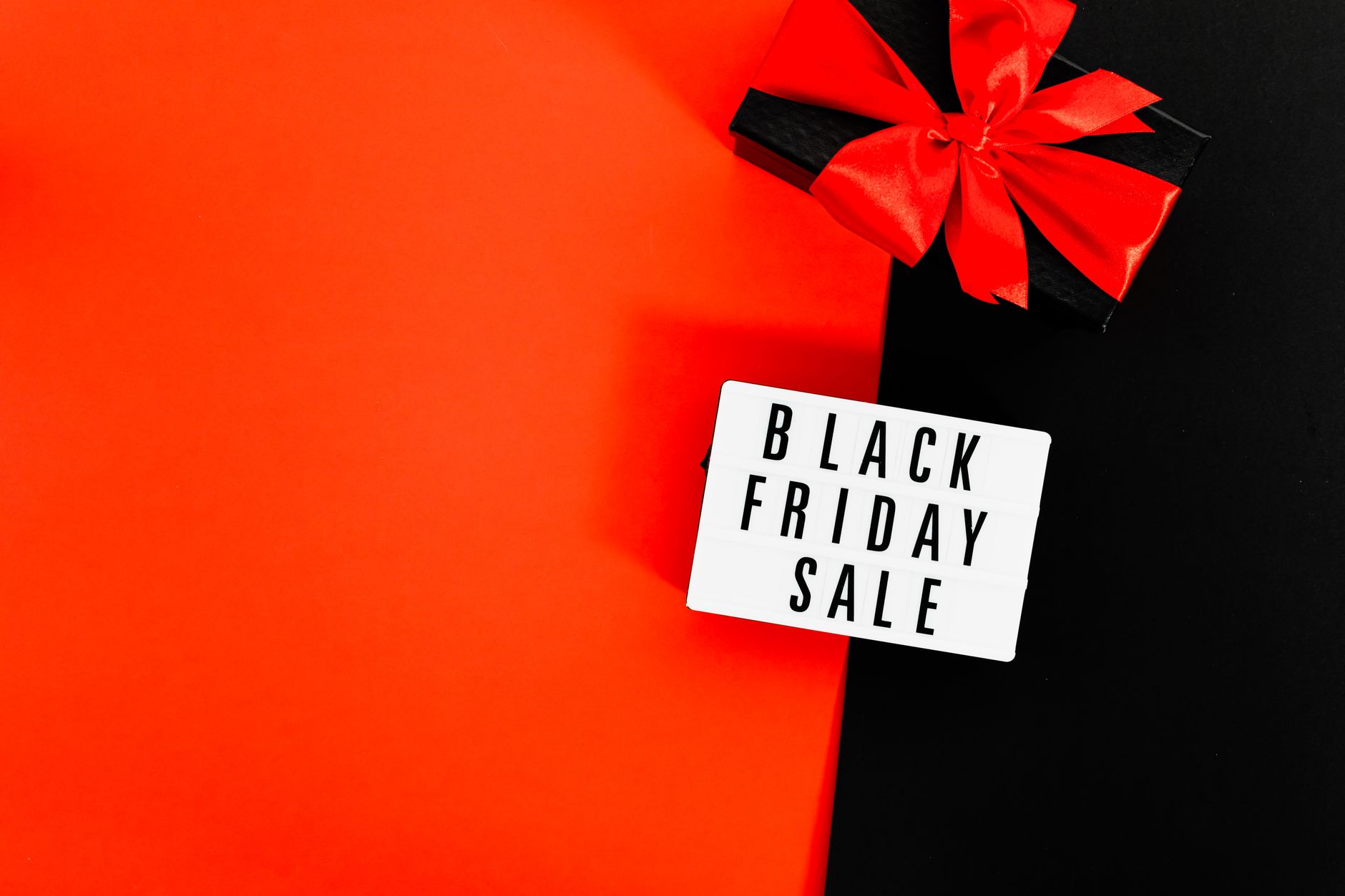 Black Friday sale sign with gift box and red ribbon on black and red background.