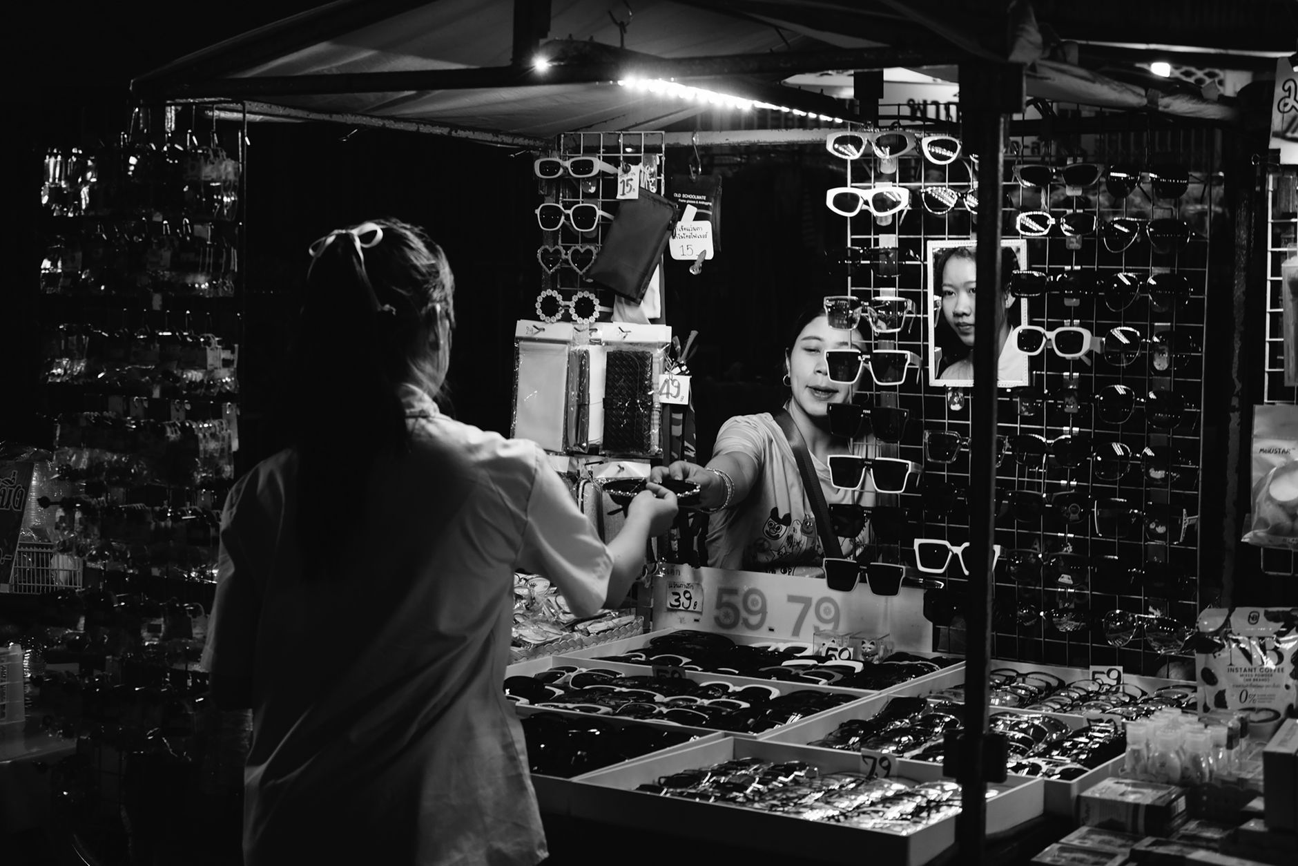A bustling night market scene with a sunglasses stall and two women interacting.