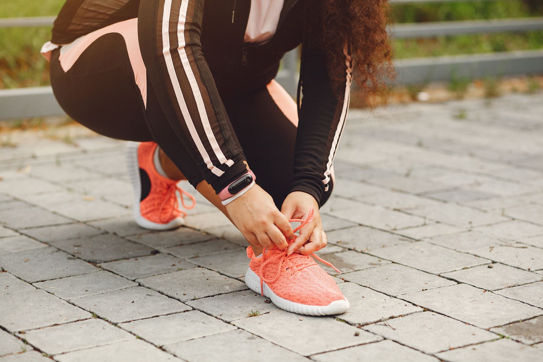 A woman tying her shoelaces on a brick walkway, ready for outdoor exercise.