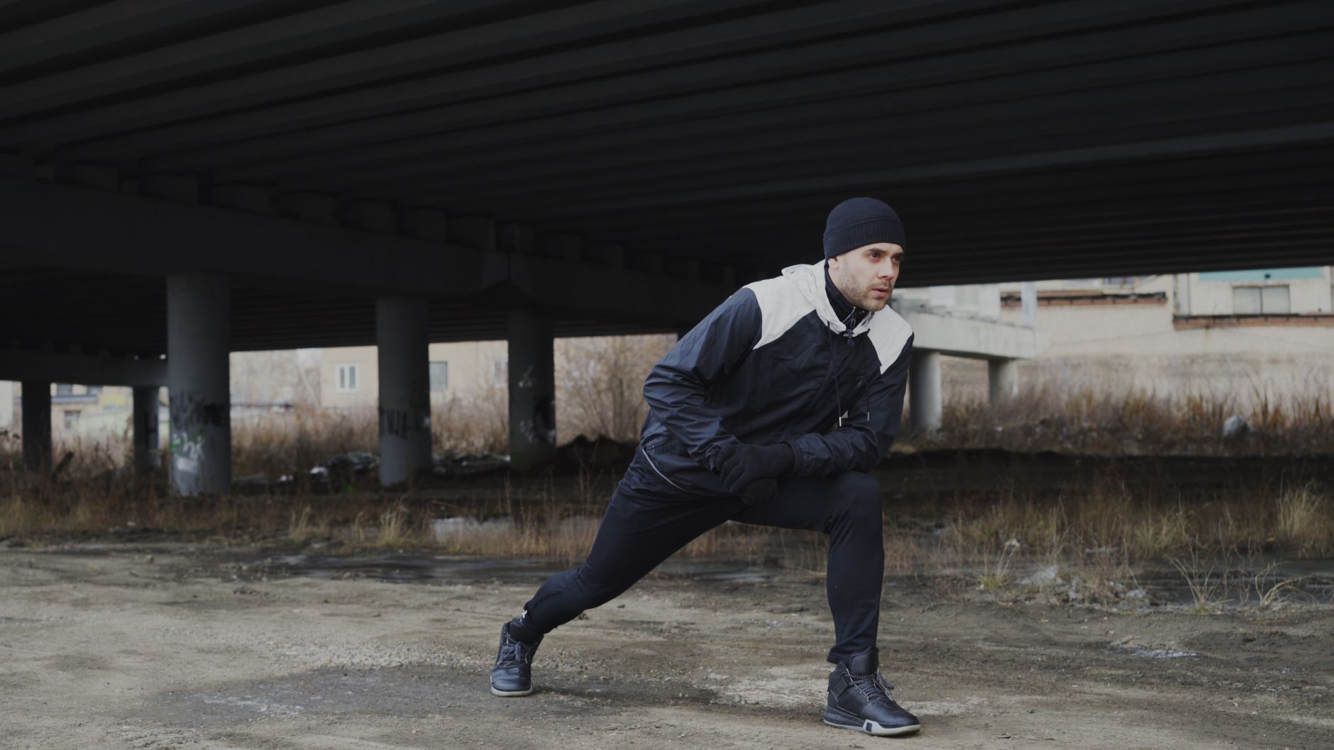 Man in sportswear stretching before jogging under a bridge.