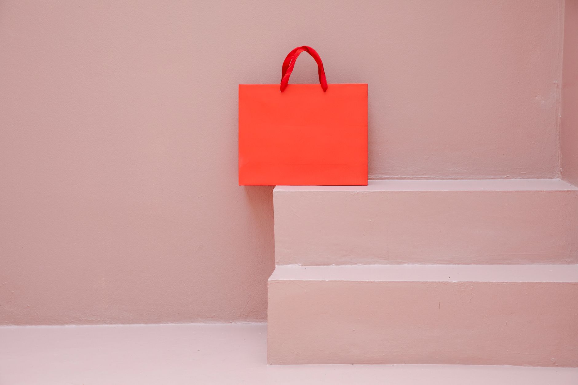 A striking orange paper shopping bag positioned on pastel pink steps, perfect for modern retail themes.