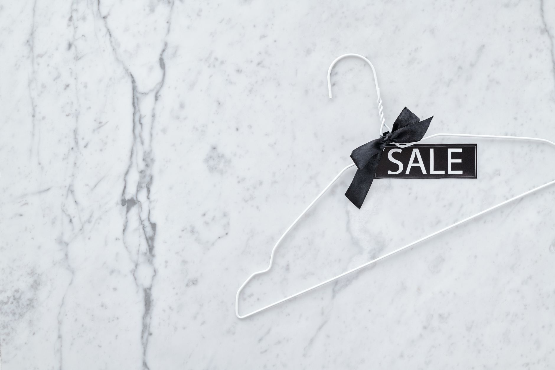 White wire hanger with a sale tag and ribbon on marble surface. Perfect for retail promotions.