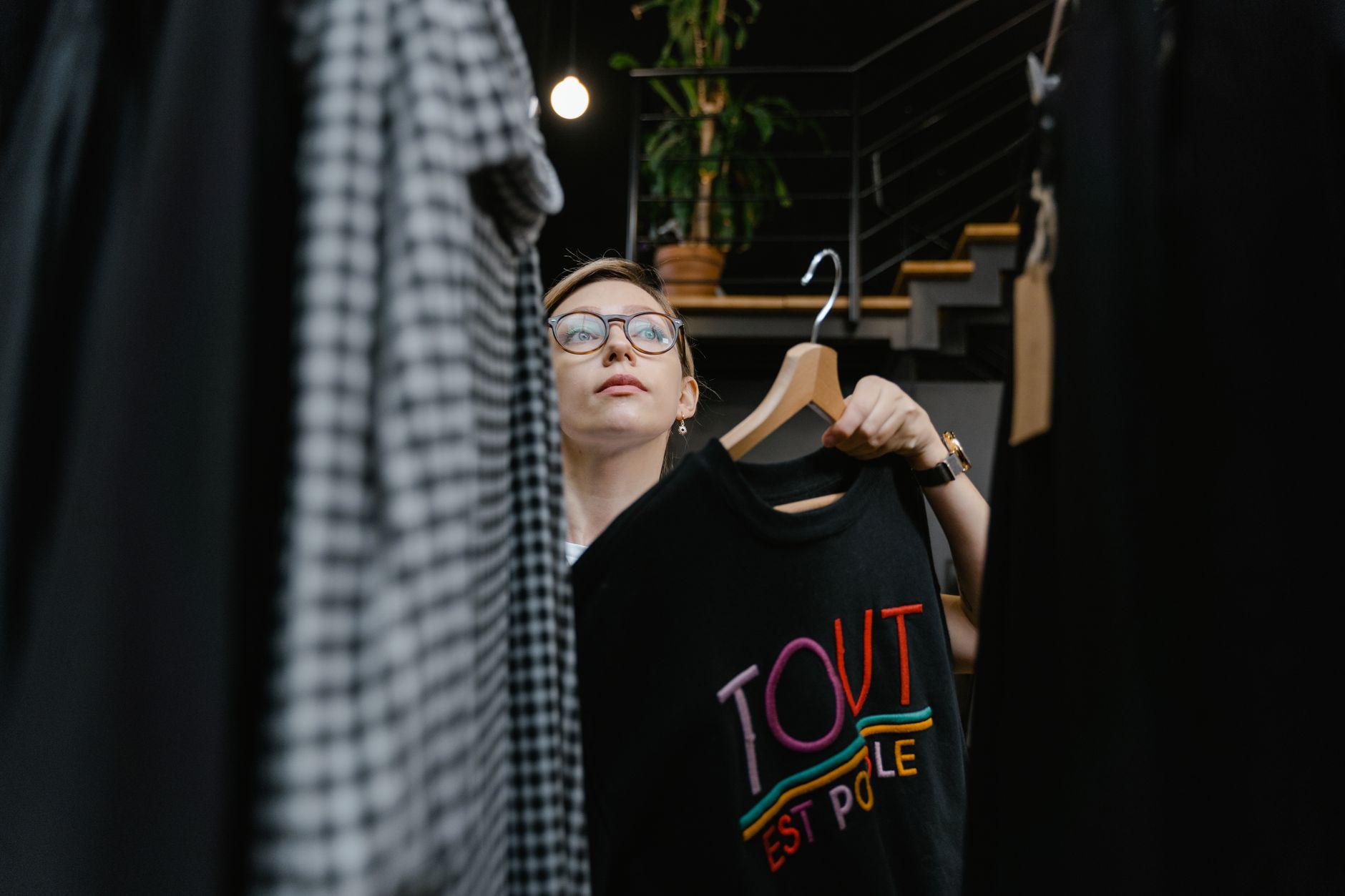 Woman holding a T-shirt on a hanger in a fashion boutique. Shopping experience indoors.