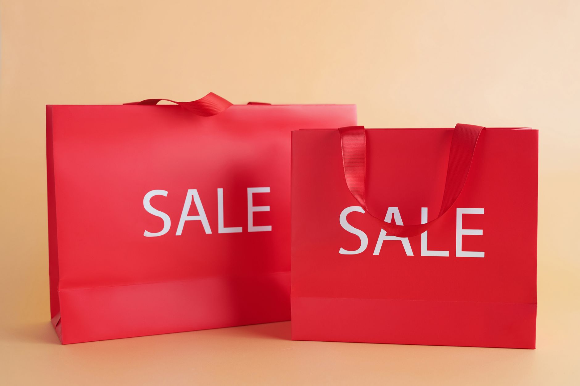 Bright red shopping bags on a neutral background with a sale text, perfect for marketing promotions.
