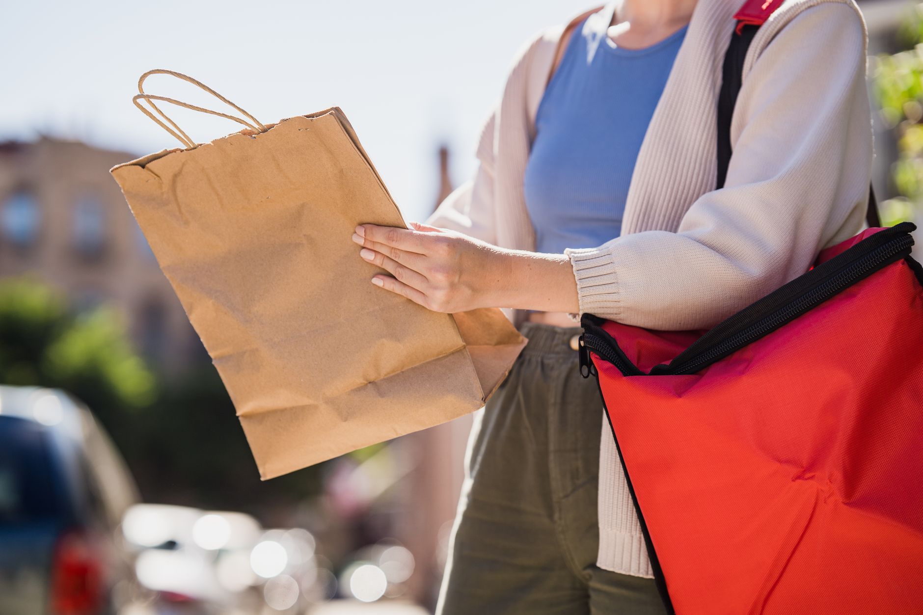 Close-up of woman holding paper bag for delivery in a sunny outdoor setting, showcasing modern lifestyle.
