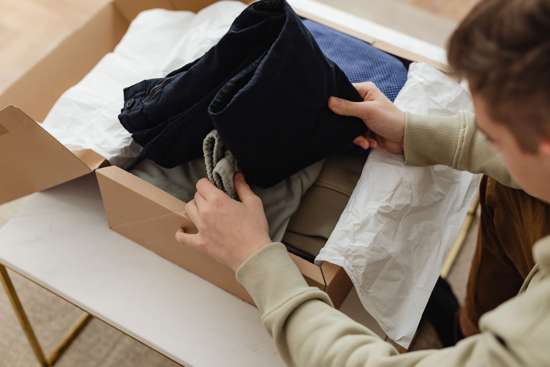 Person unpacking clothes from a delivery box indoors, showcasing a range of garments.