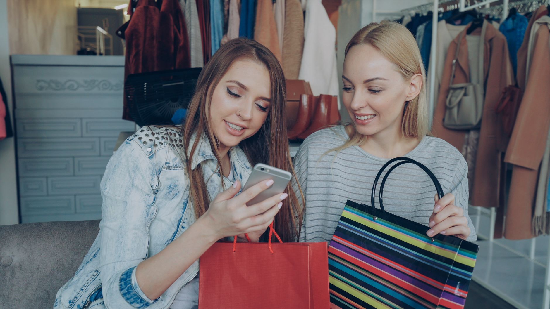 Two women enjoying shopping together, sharing content on a phone in a stylish boutique.