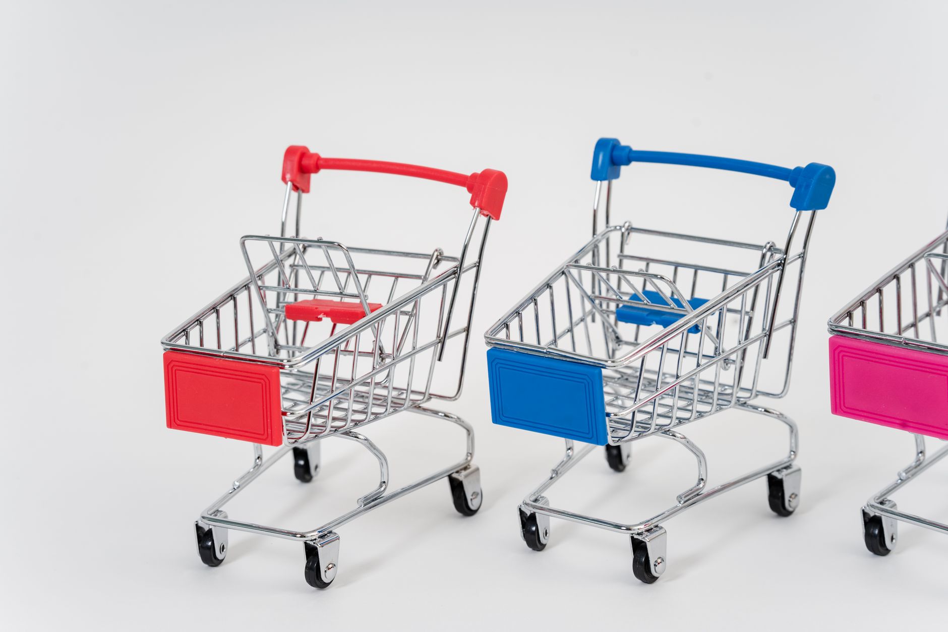Close-up of three colorful miniature shopping carts in red, blue, and pink.