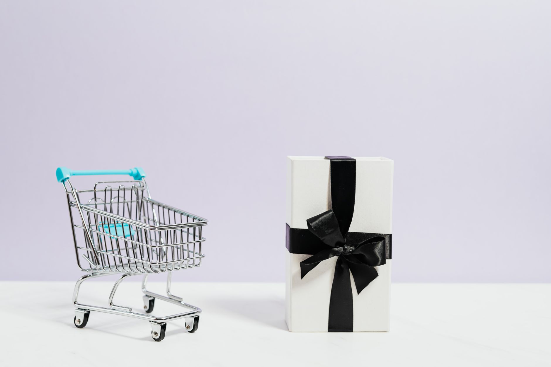 Minimalist shopping concept with cart and gift box tied with black ribbon.