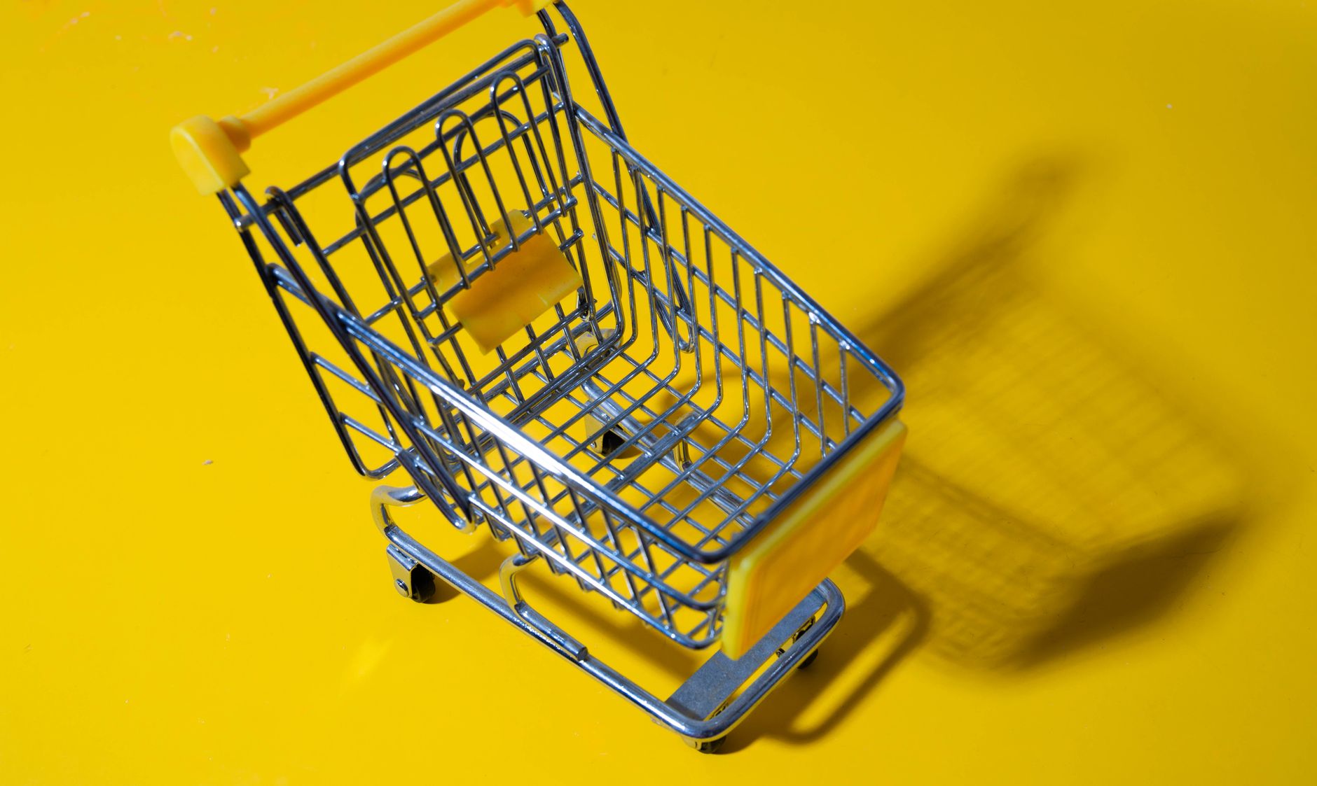 A toy shopping cart displayed against a vivid yellow background, casting a shadow.