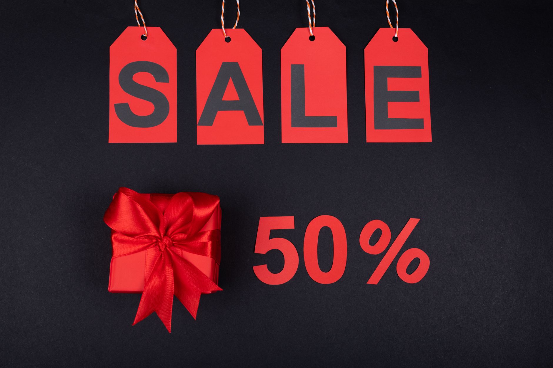 Red sale tags and gift box on black background emphasizing 50% discount for promotions.