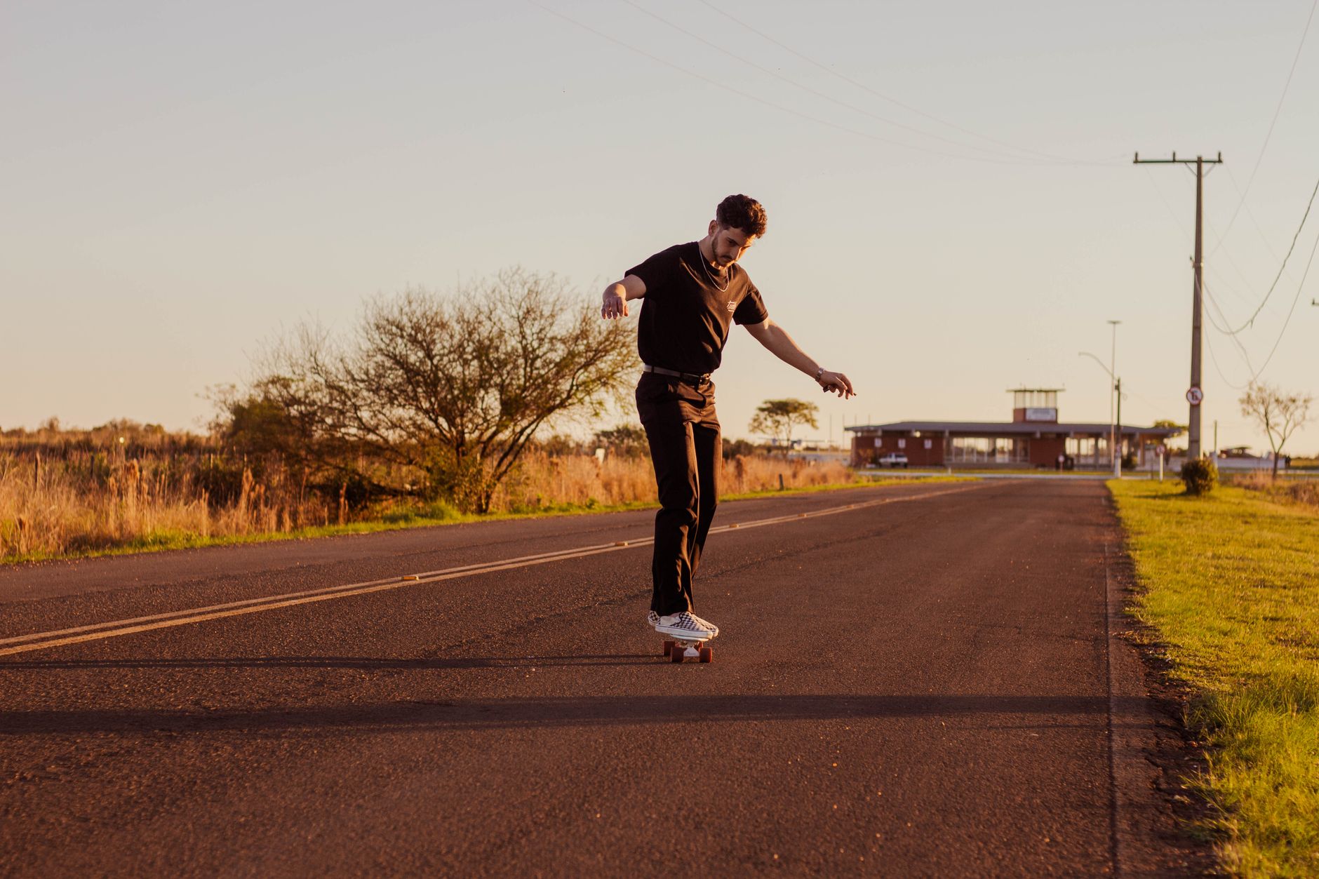 A young man skateboarding on a rural road during the day, showcasing balance and outdoor adventure.