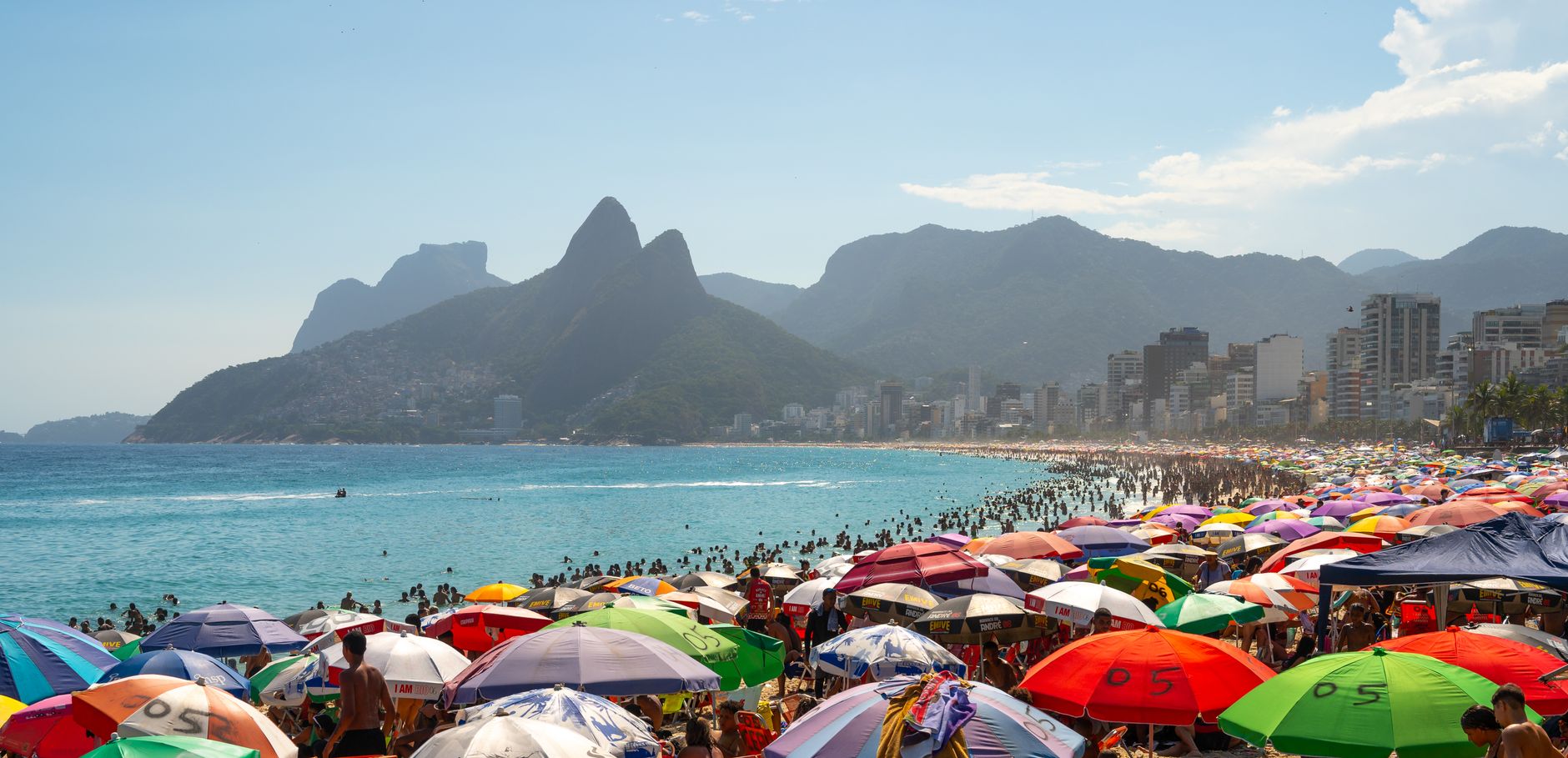 Colorful umbrellas and crowds on Ipanema Beach with stunning mountain views in Rio de Janeiro, Brazil.