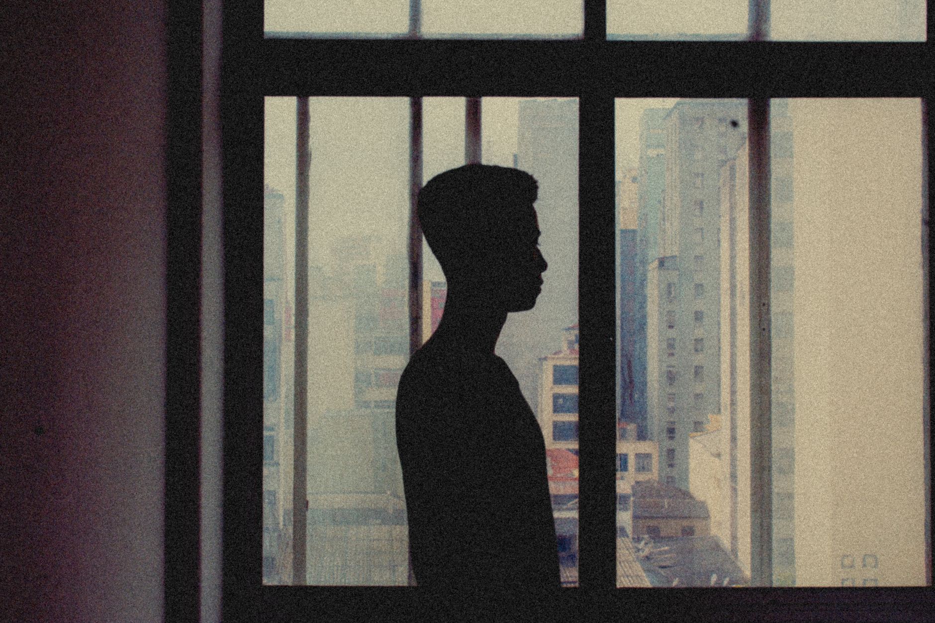 Silhouette of a person looking out a city apartment window showcasing an abstract urban landscape.