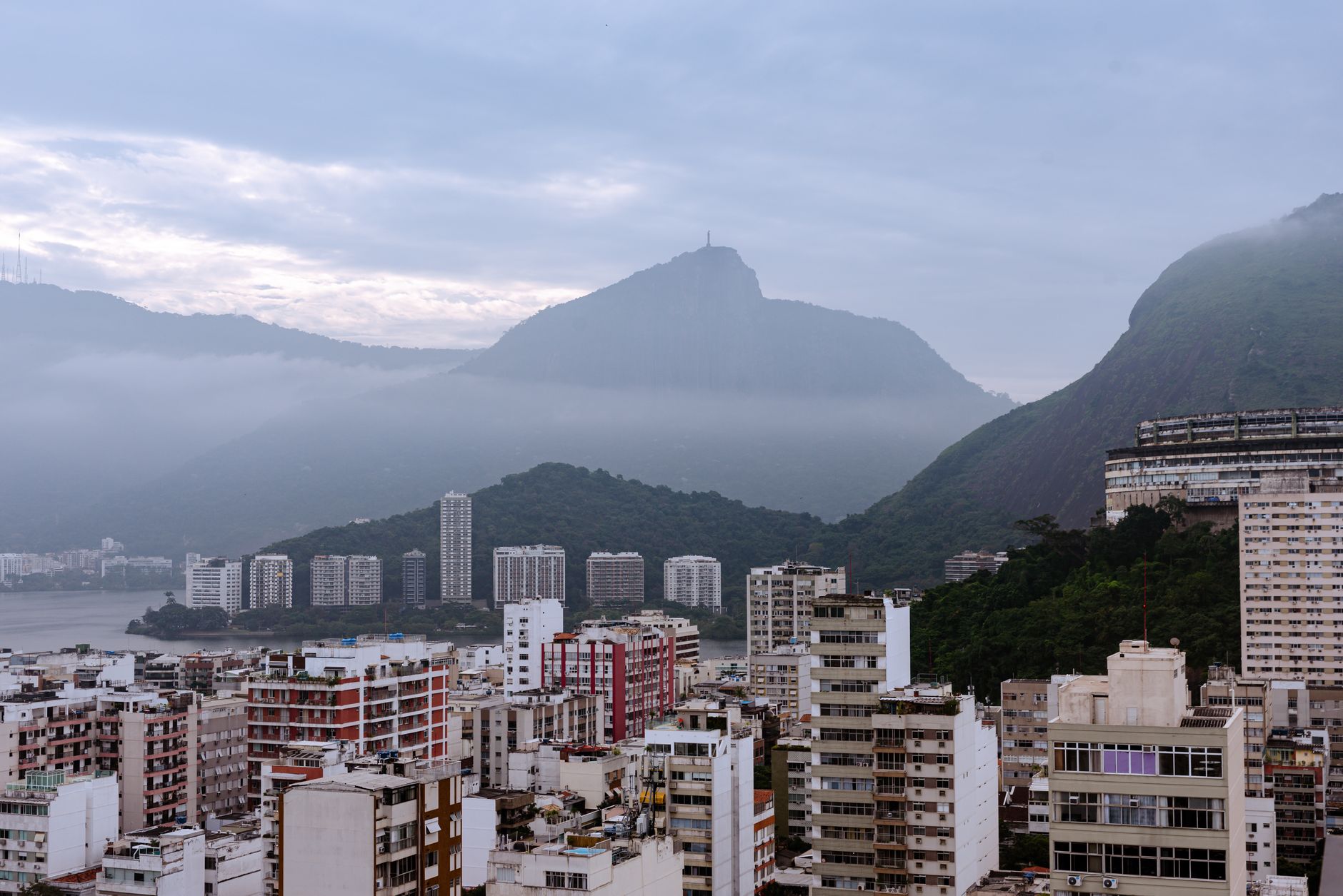 Panoramic view of Rio de Janeiro skyline with mountains and misty clouds in the background at dawn.