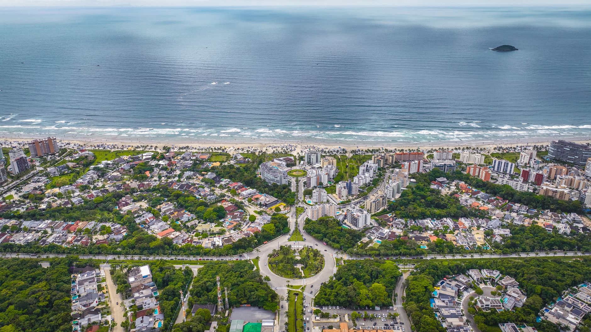 Aerial view of a coastal city with lush greenery, buildings, and a wide beach.