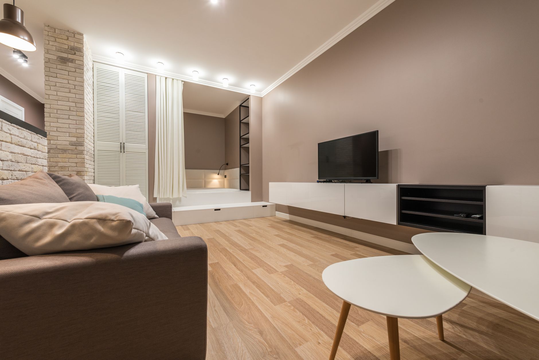 Comfortable couch with cushions placed against wall with modern TV in living room with tub and curtain in light apartment