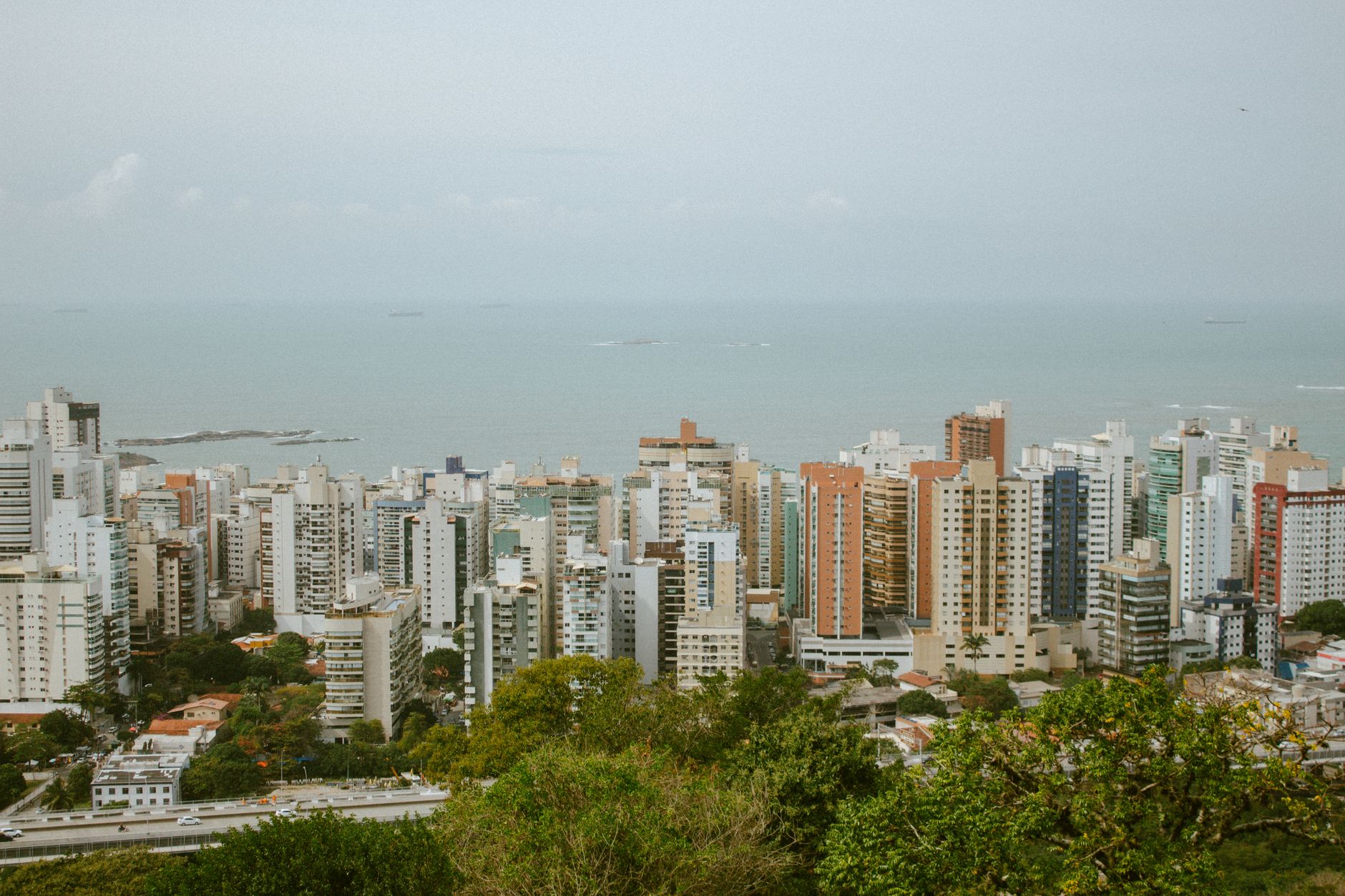 Scenic view of urban skyline in ES, Brazil with ocean in the background, showcasing towering buildings and lush greenery.