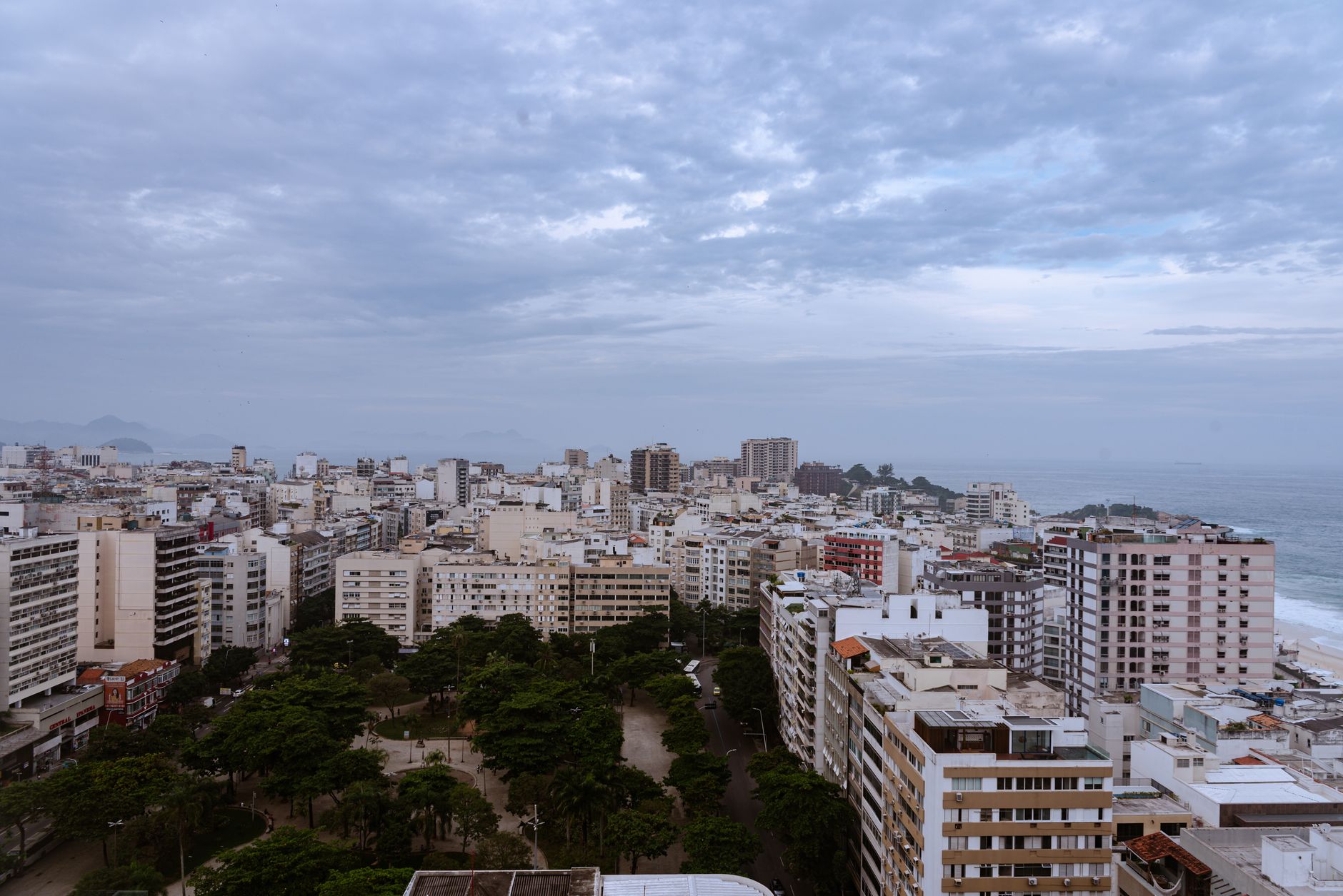 Aerial view of Rio de Janeiro's cityscape with coast and cloudy sky.