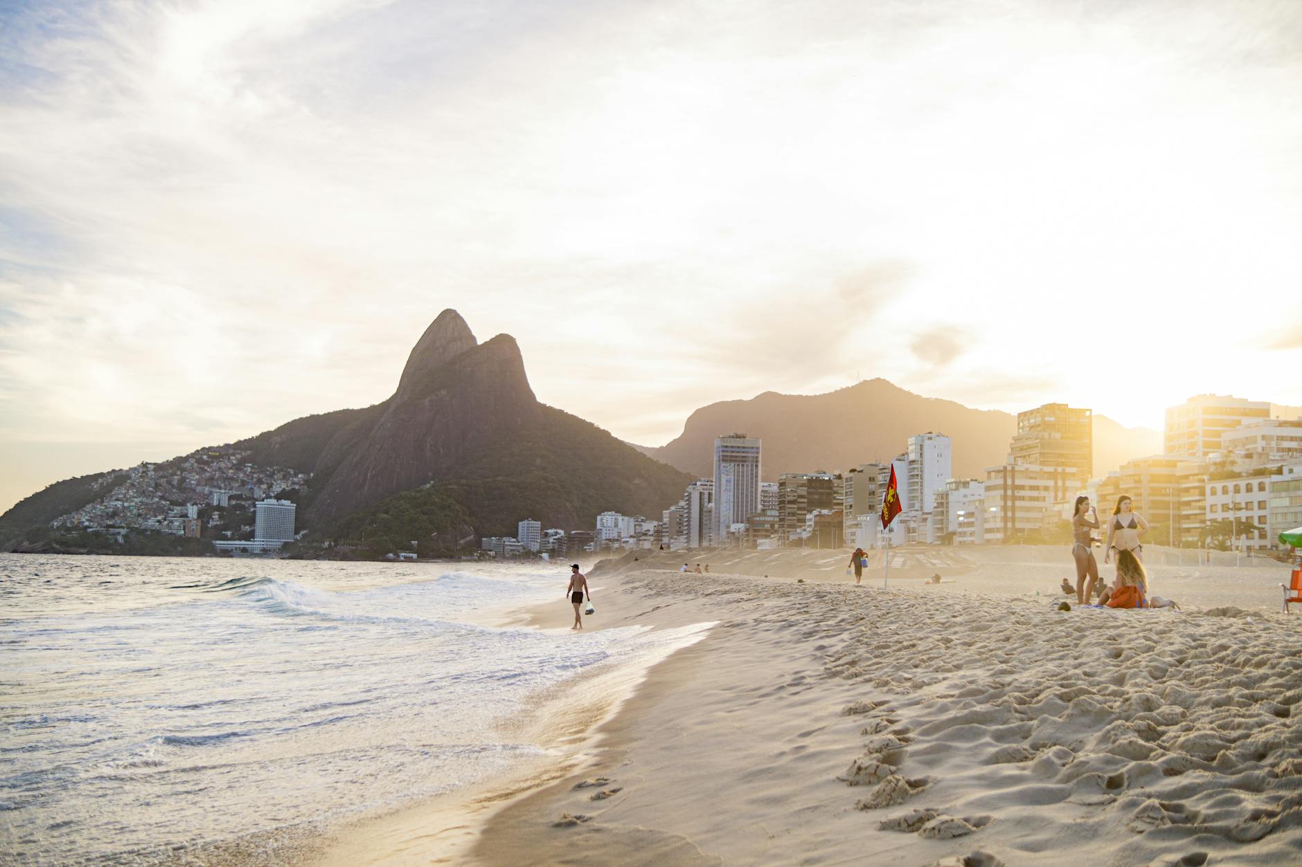 Golden sunset over vibrant Ipanema Beach with mountains and cityscape.