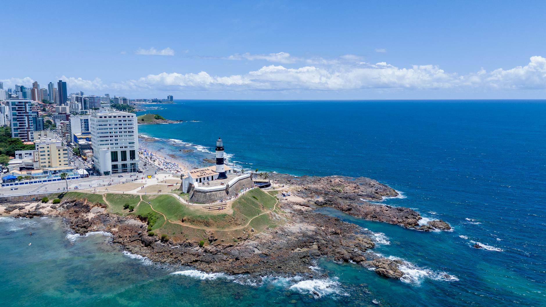 Stunning aerial view of the iconic Barra Lighthouse in Salvador, Brazil, against a vibrant ocean backdrop.