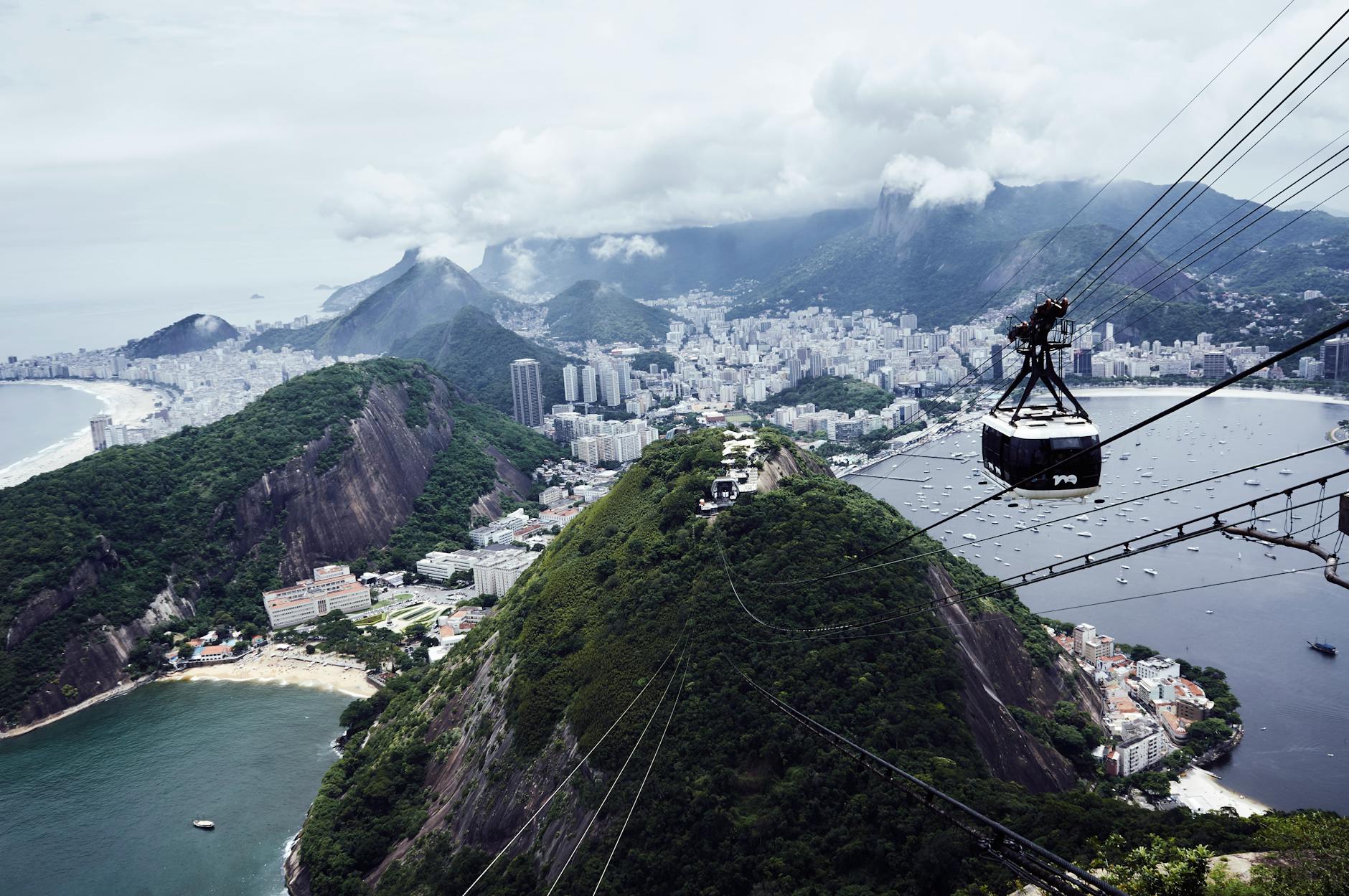 Cable car ascending Sugarloaf Mountain with panoramic view of Rio de Janeiro's coastline and skyline.