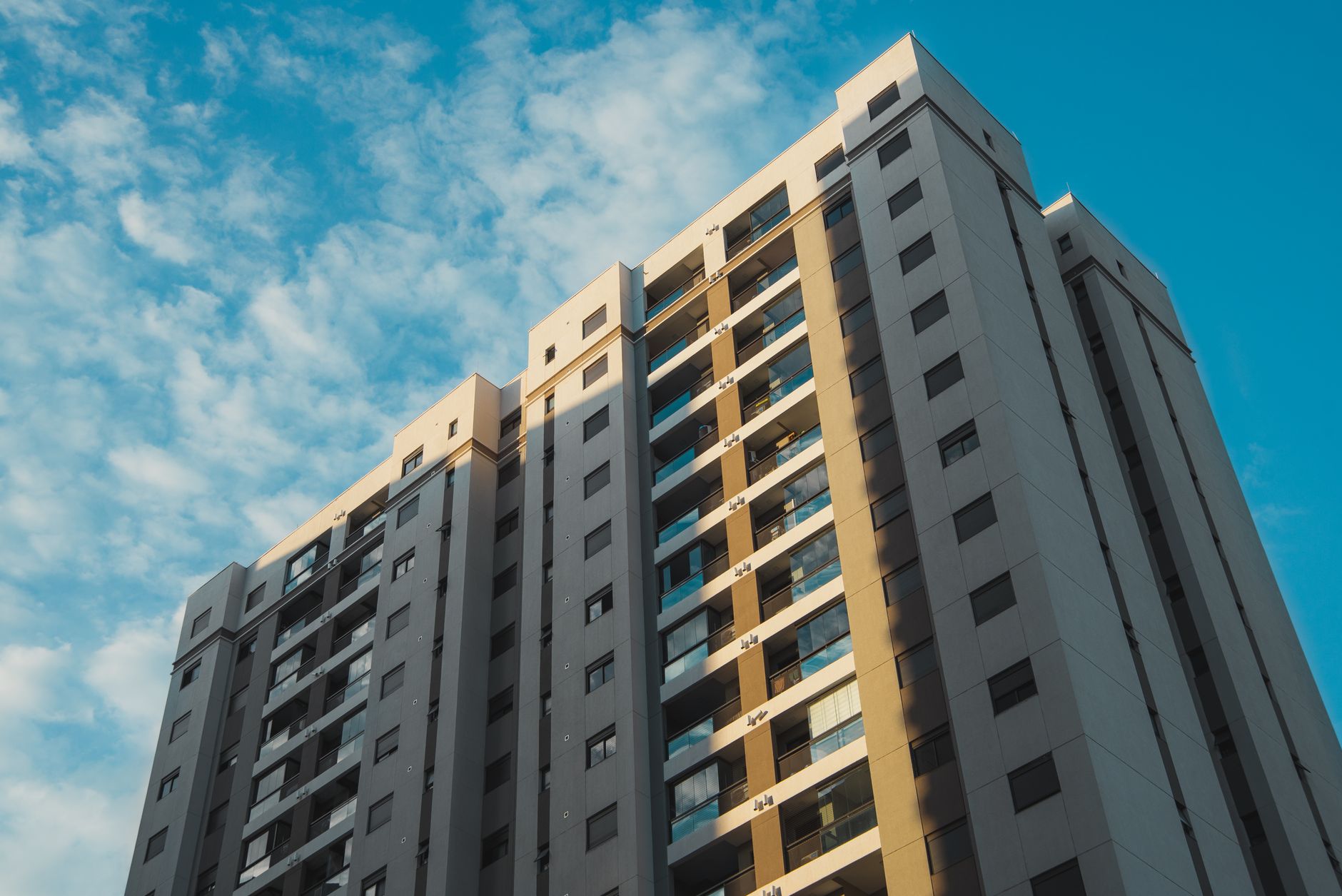 View of a modern residential skyscraper with a clear blue sky backdrop, shot from a low angle.