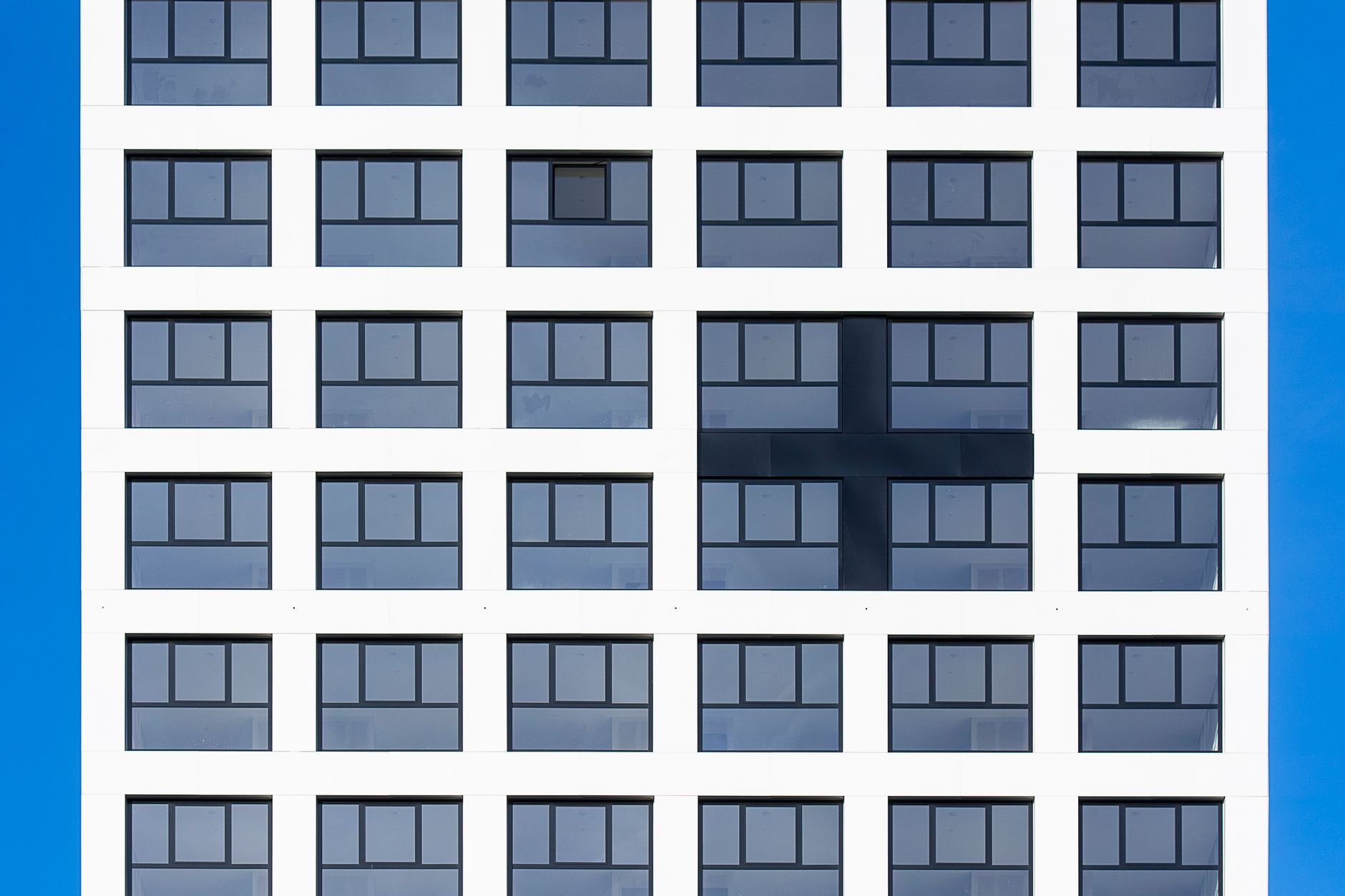 Symmetrical building facade with unique cross pattern, blue sky backdrop.