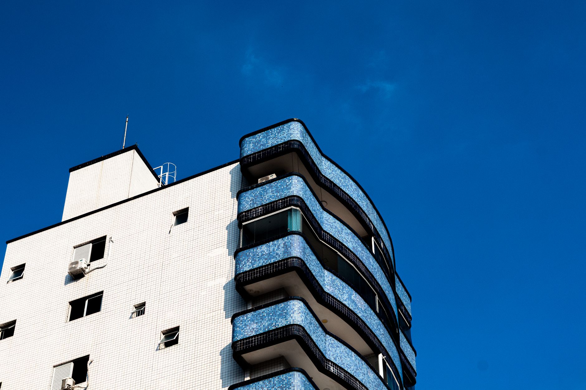 A modern architecture building featuring blue balconies and a clear blue sky.