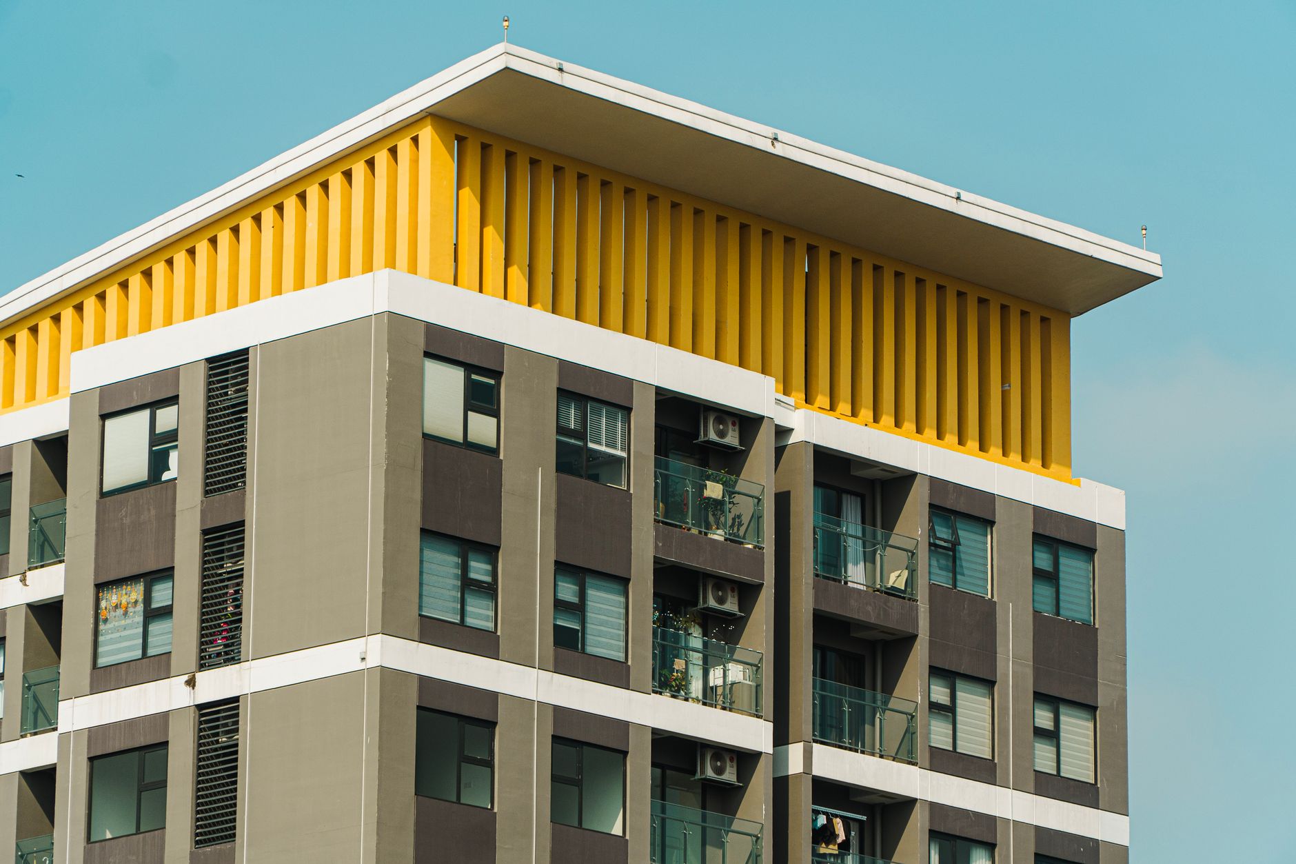 Contemporary apartment building featuring striking yellow architectural elements set against a clear blue sky.