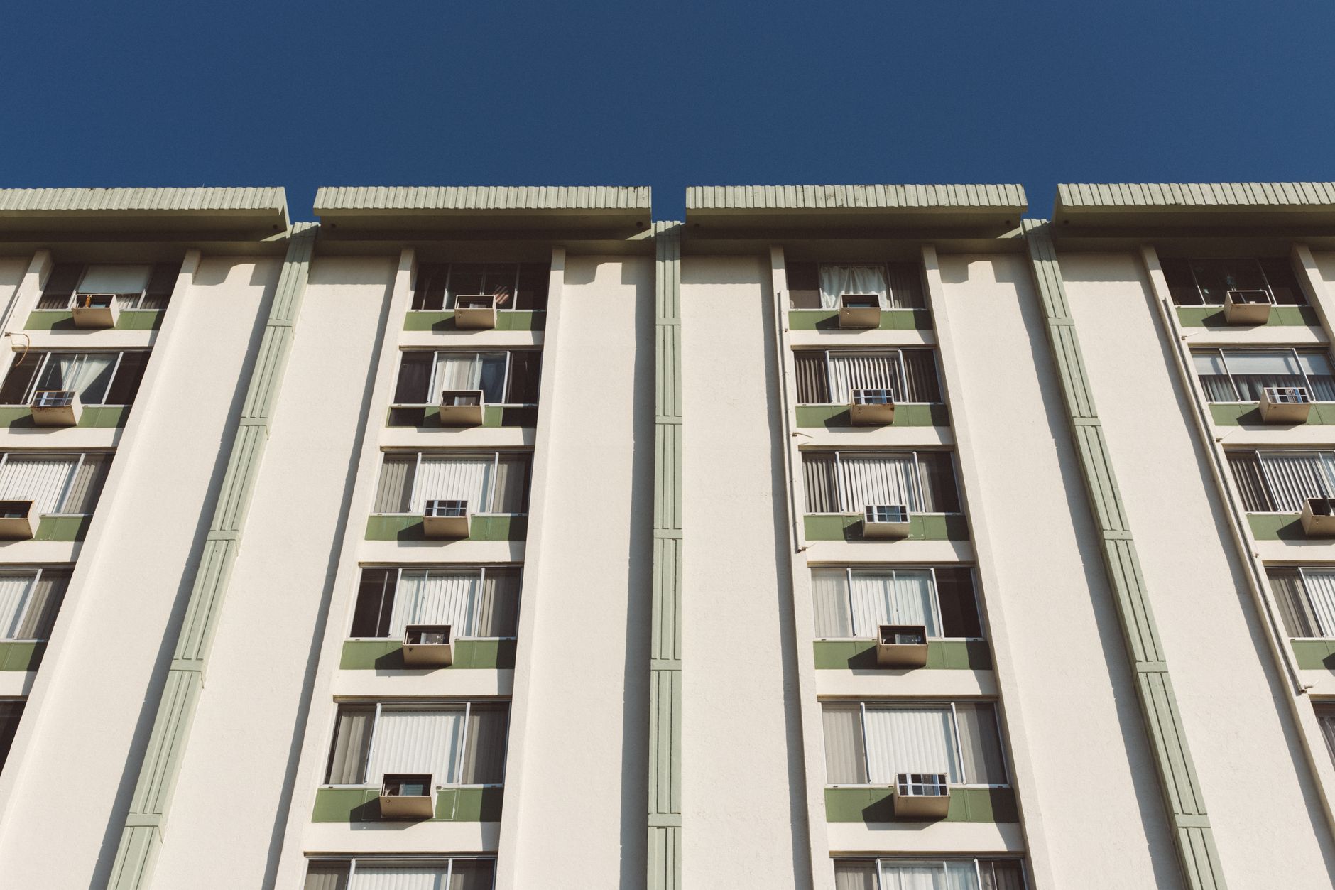 Low angle view of a residential building facade with air conditioning units and windows.