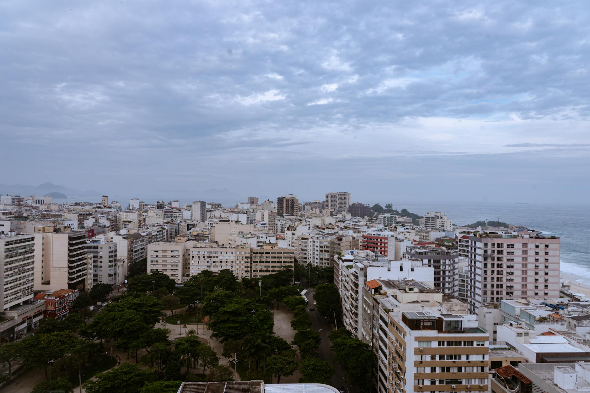 Aerial view of Rio de Janeiro's cityscape with coast and cloudy sky.