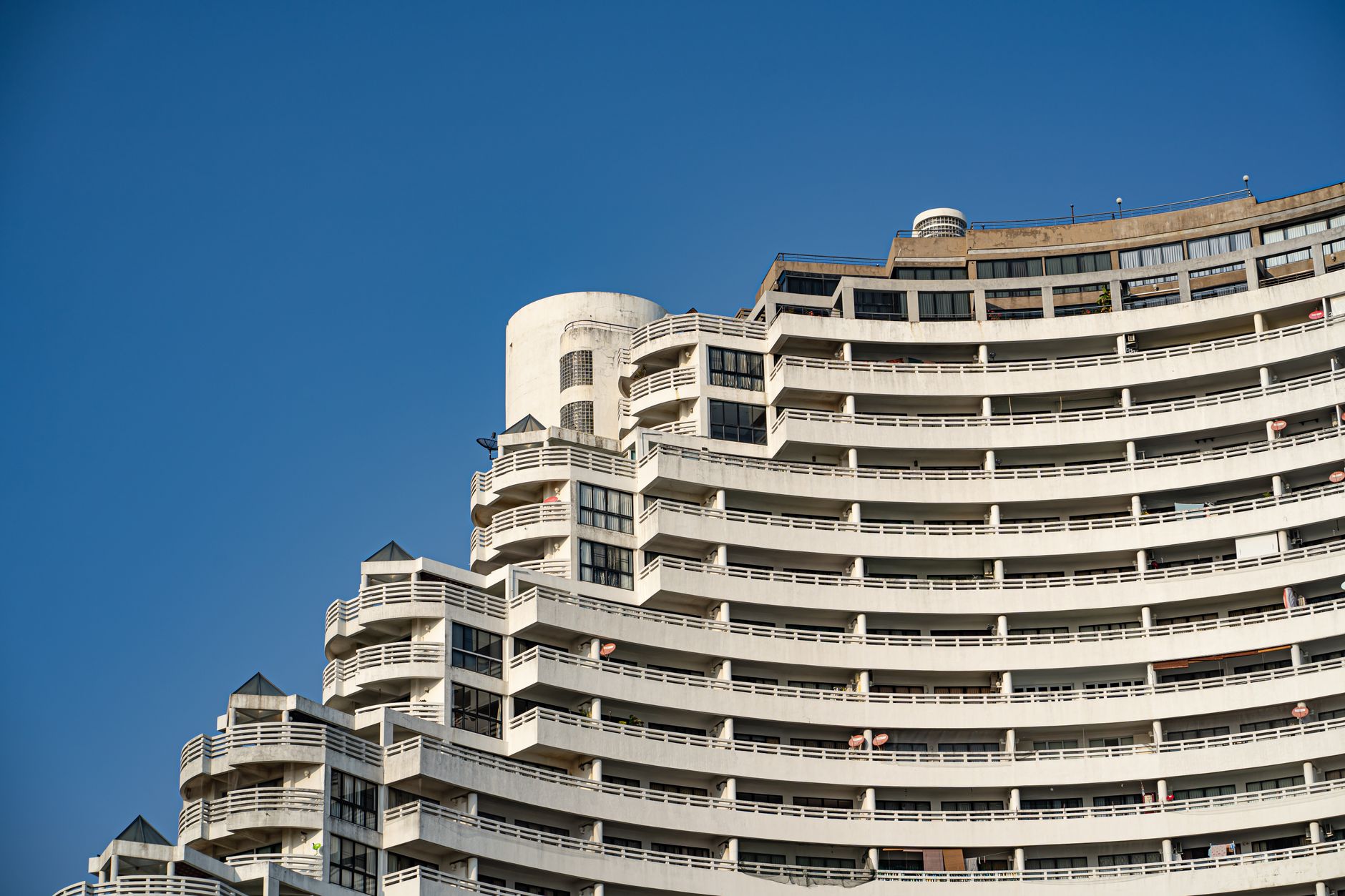 Contemporary high-rise building with curved balconies and glass windows under a clear blue sky.