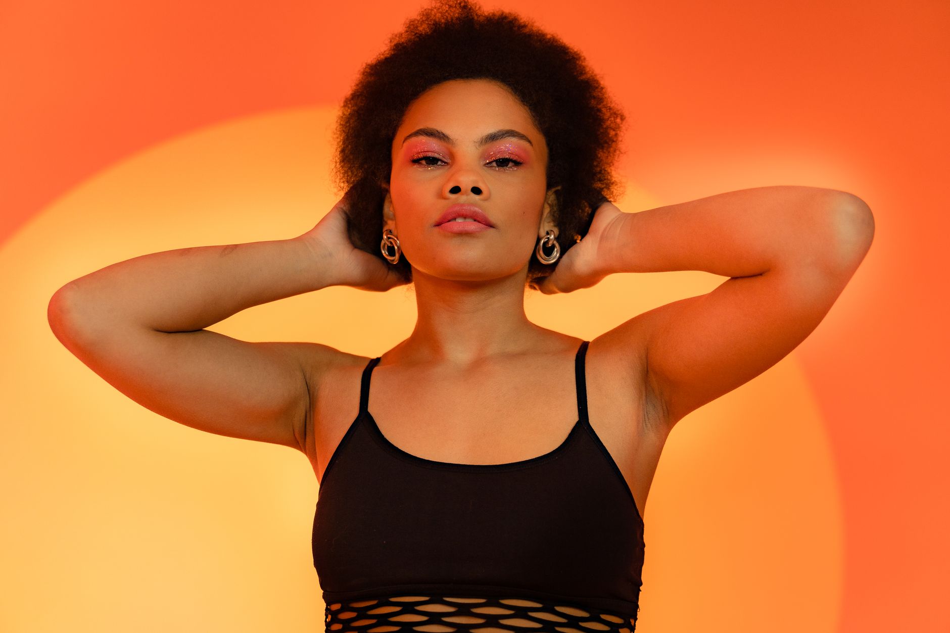 Confident black woman with afro hair posing against a vibrant orange background in a studio shoot.