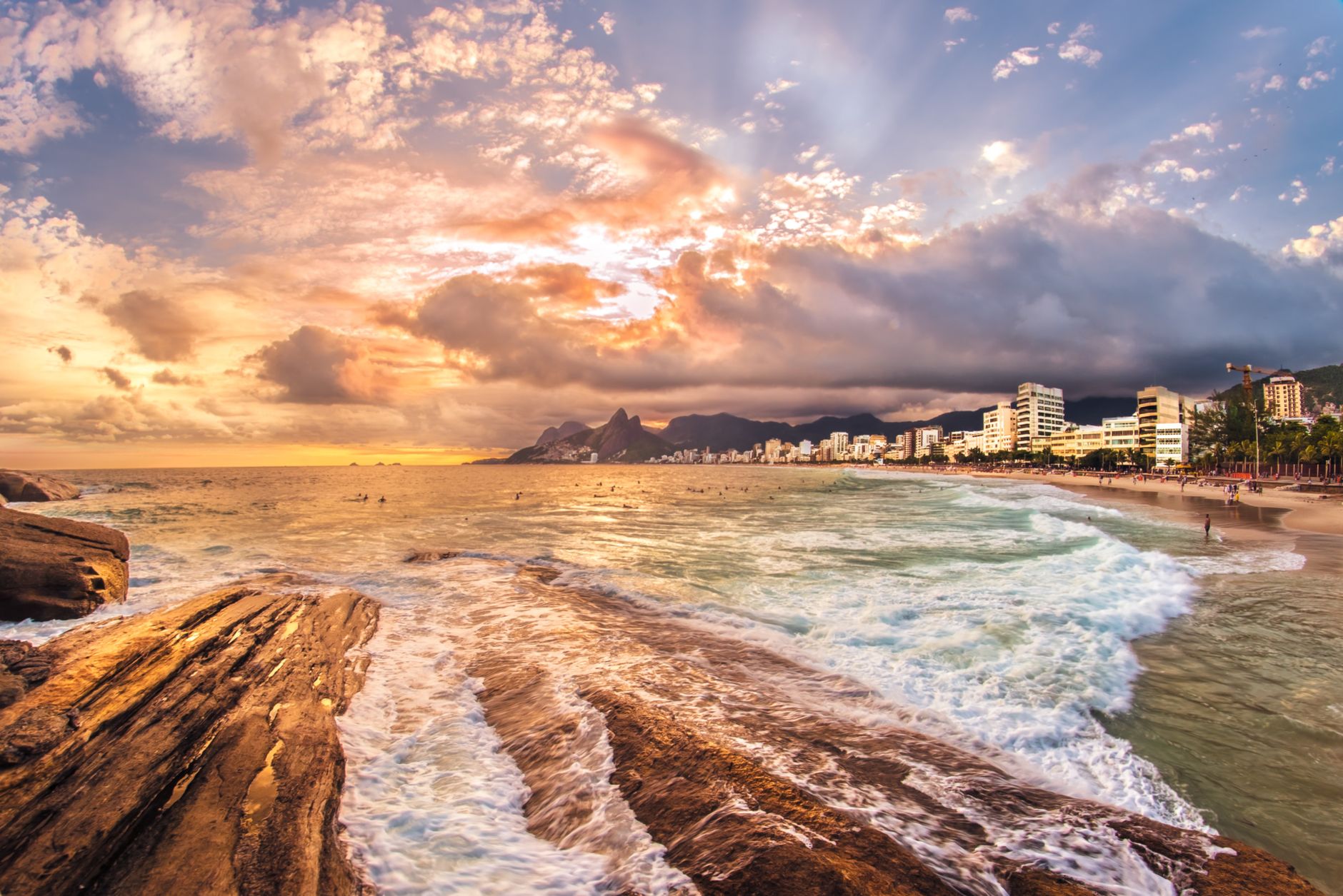 Picturesque seascape with foamy waves washing sandy beach against cloudy sky at sunset time with buildings located in distance in summer