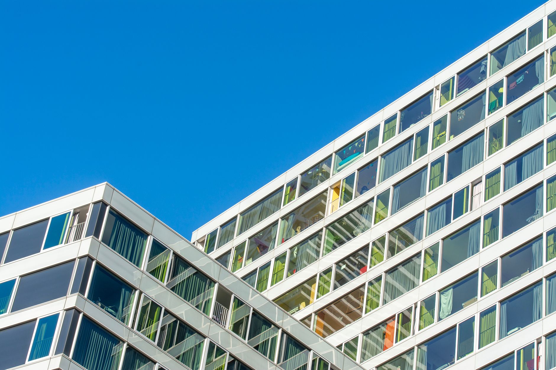 Contemporary glass facade of a modern building in Den Haag against a clear blue sky.