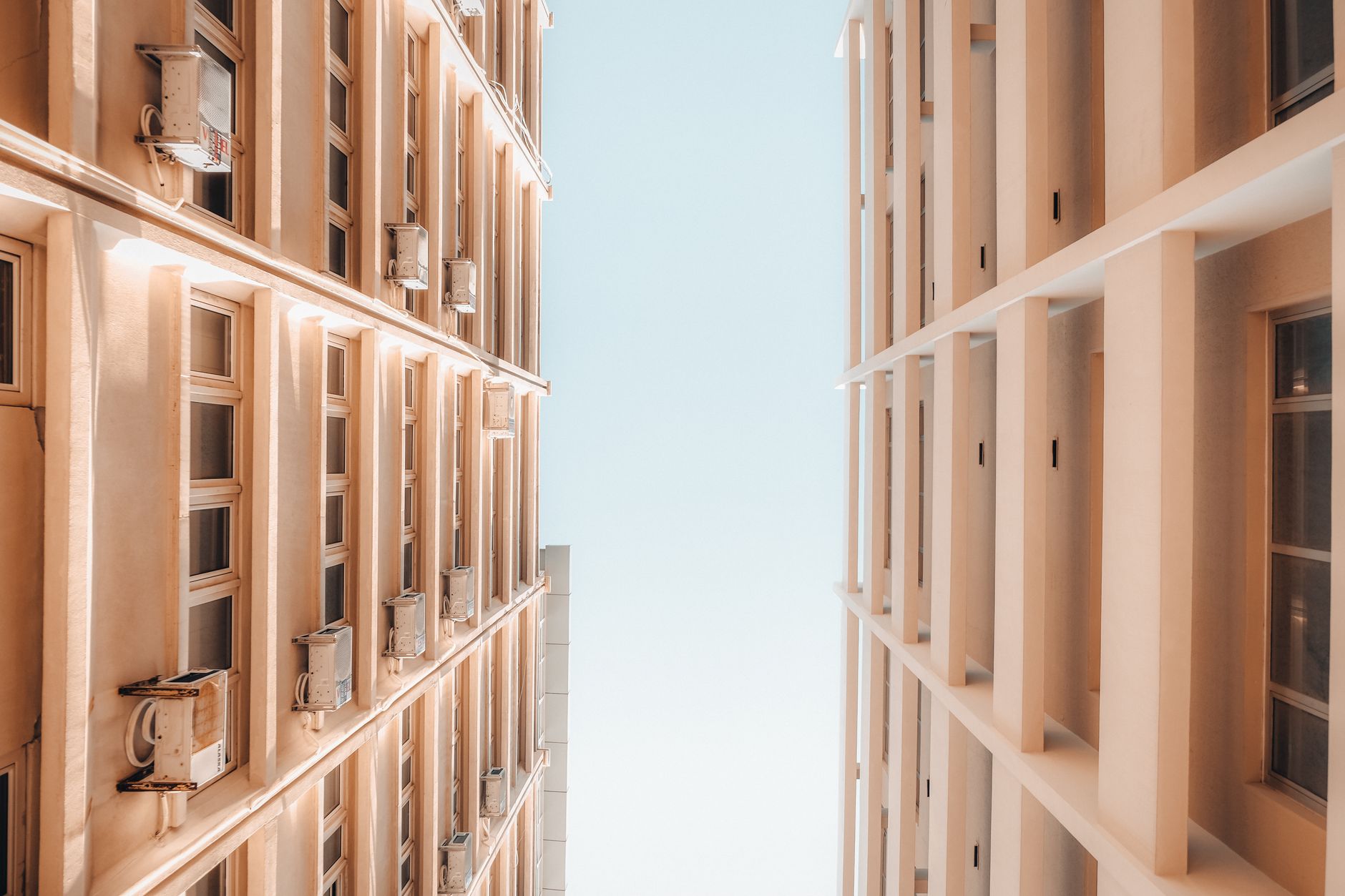 Low-angle view of modern building exteriors with windows and AC units against clear blue sky.