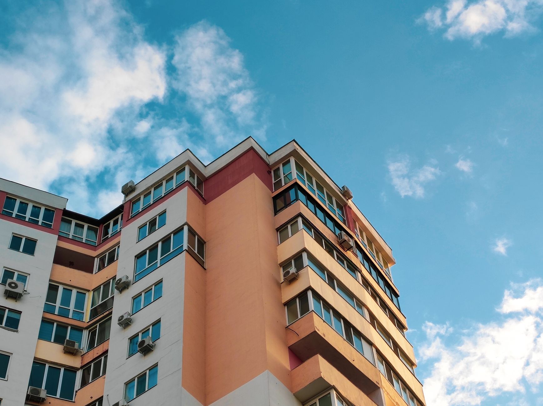 Urban residential building with balconies and air conditioning against a clear blue sky.