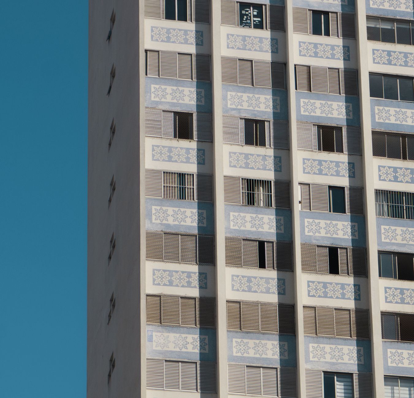 Close-up of a tall building with geometric patterns and open windows against a clear blue sky.