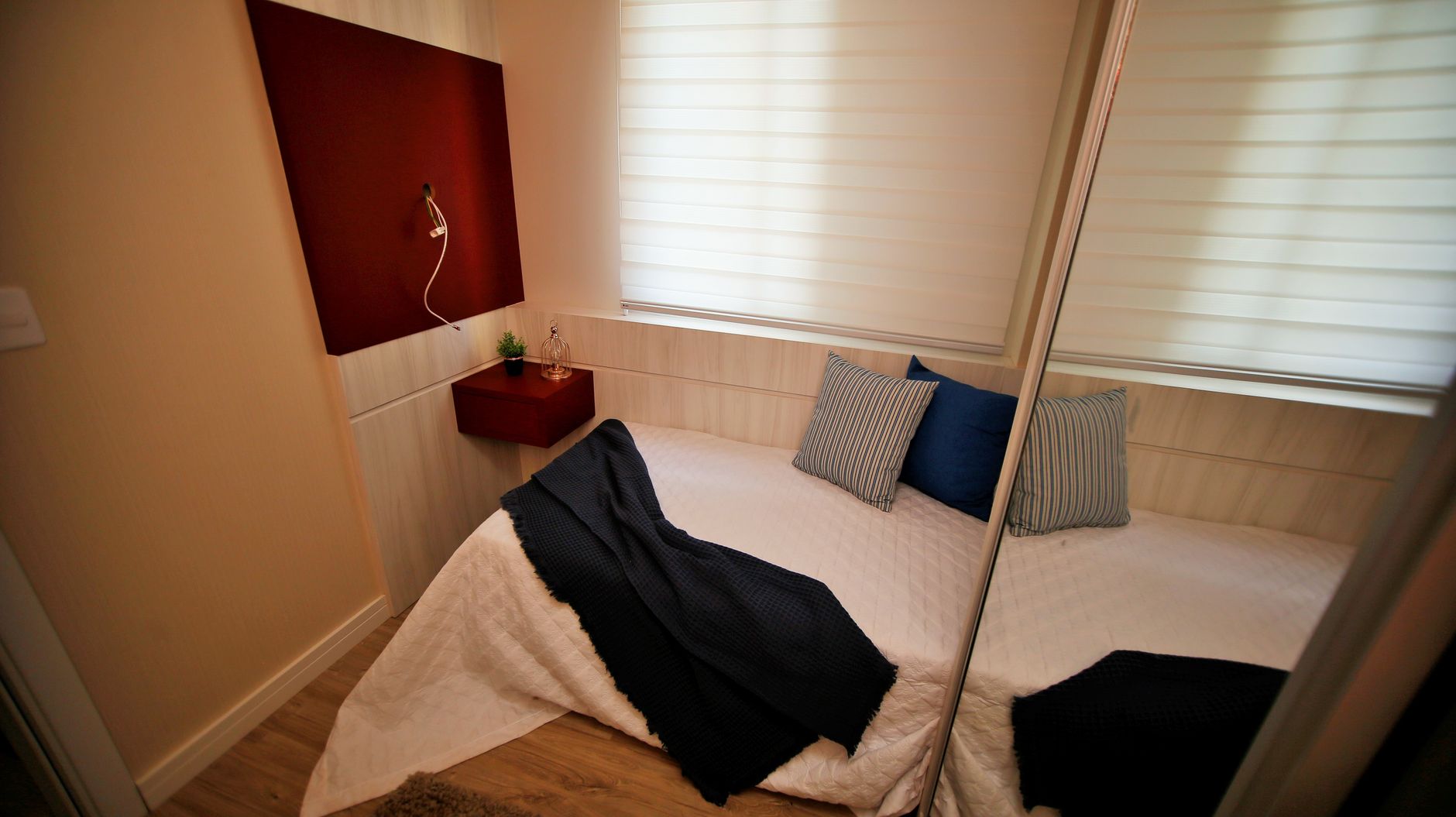 Small cozy bedroom with minimalist decor, featuring a mirror and soft lighting.