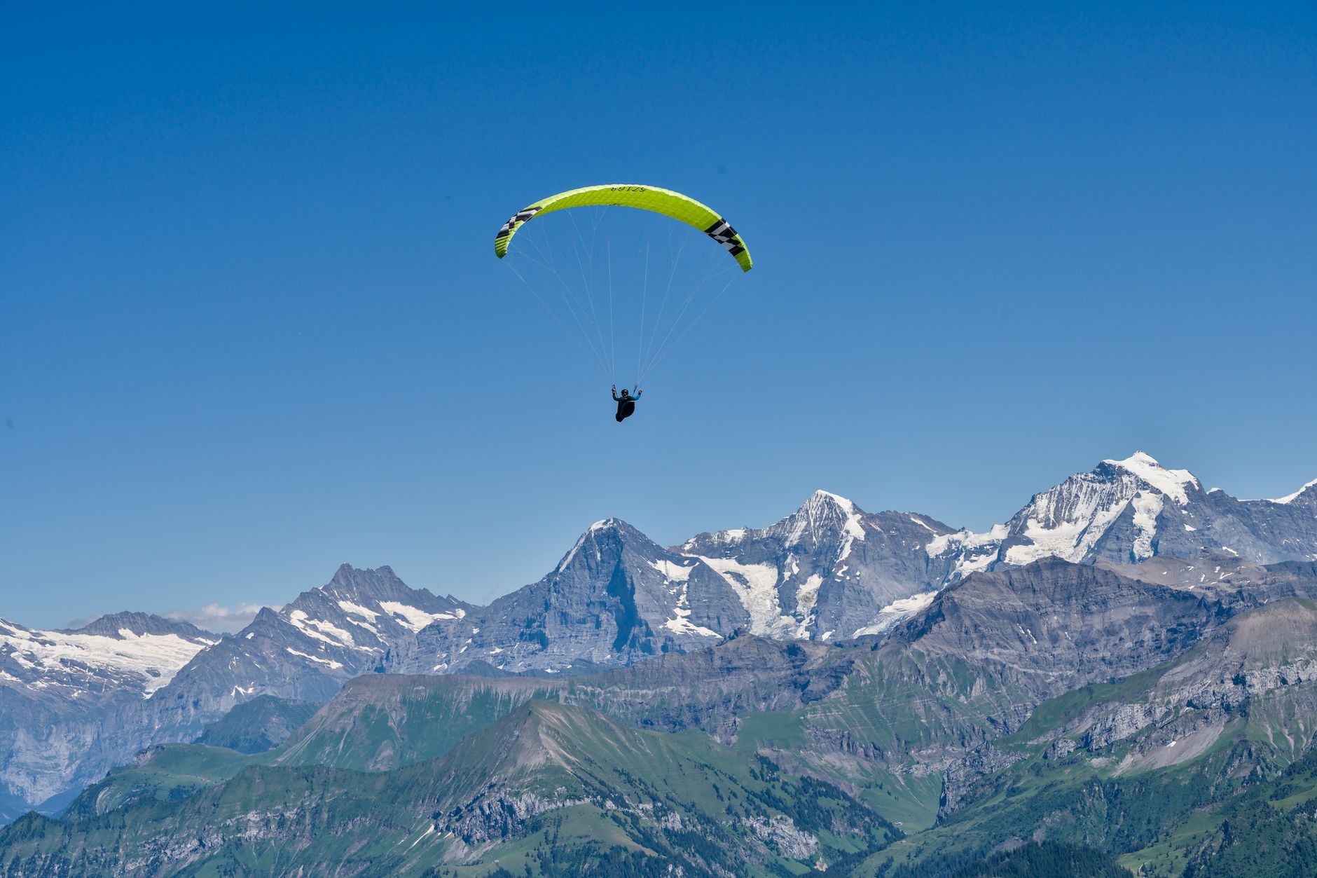 Paraglider soaring over the stunning Swiss Alps on a clear summer day.