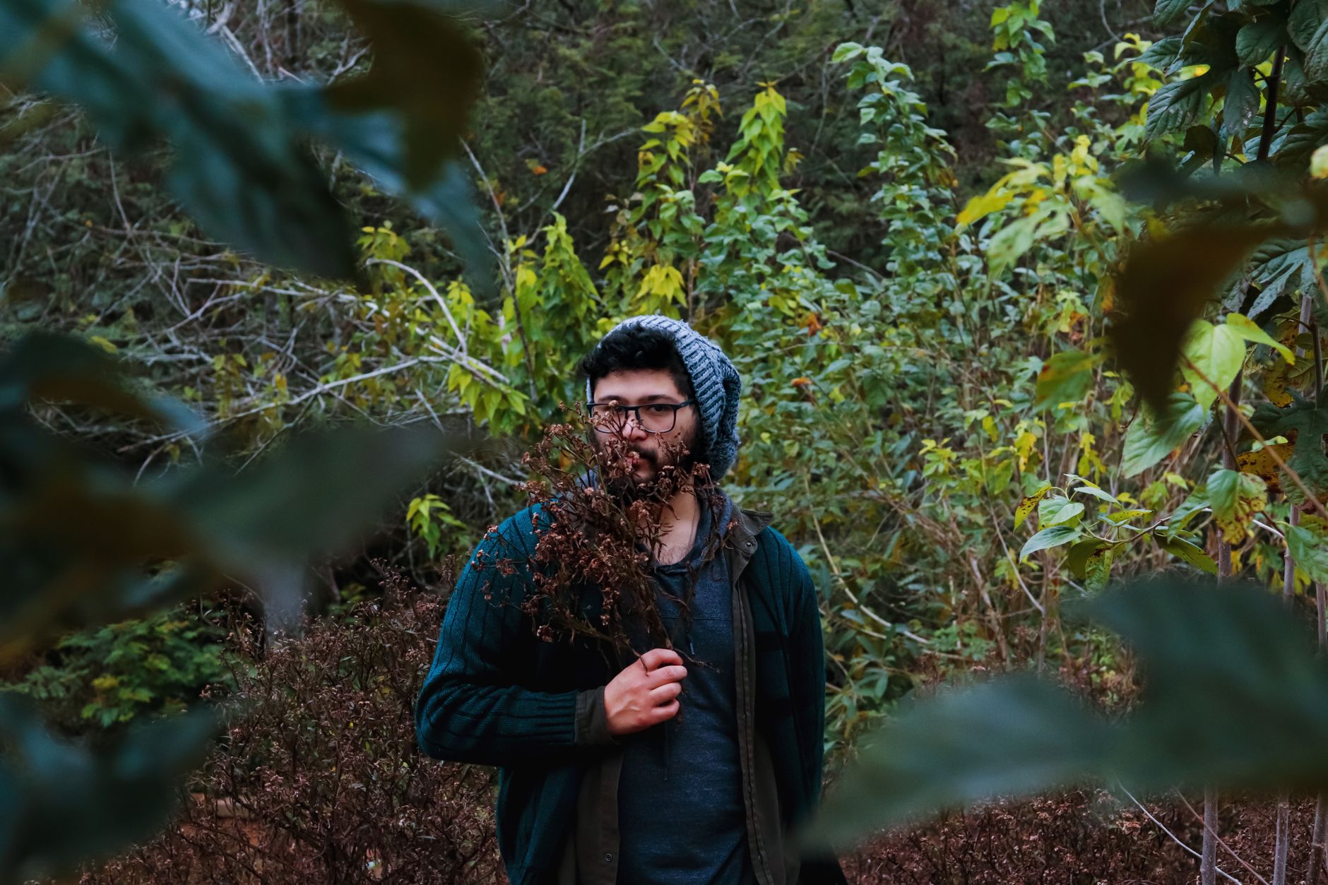 A man in a forest clearing in Taquara, Brazil, holding dry flowers with lush greenery in the background.