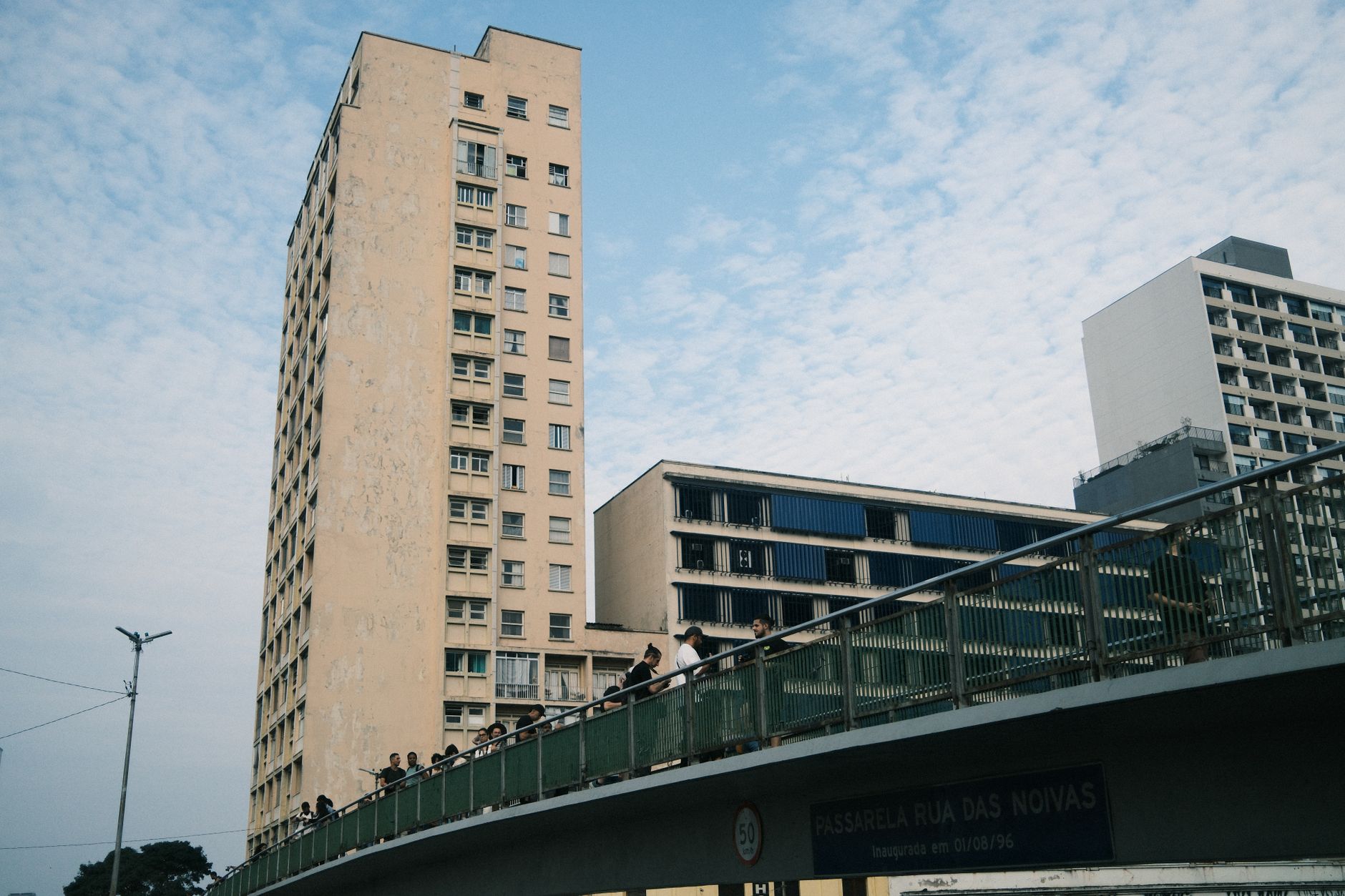 Street view of tall buildings and pedestrian bridge under a partly cloudy sky.