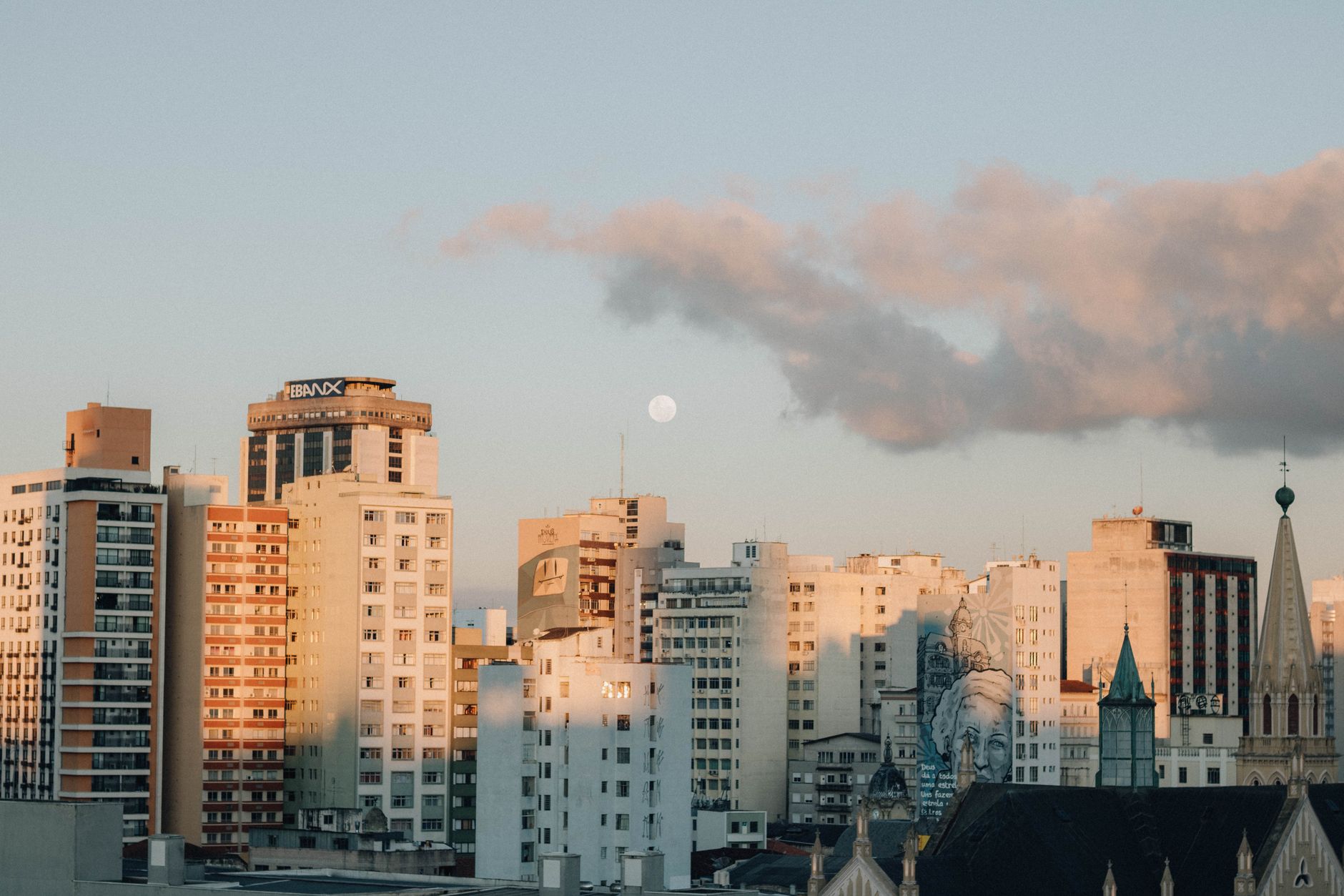 Beautiful city skyline with high-rise buildings at sunset with a cloudy sky and visible moon.