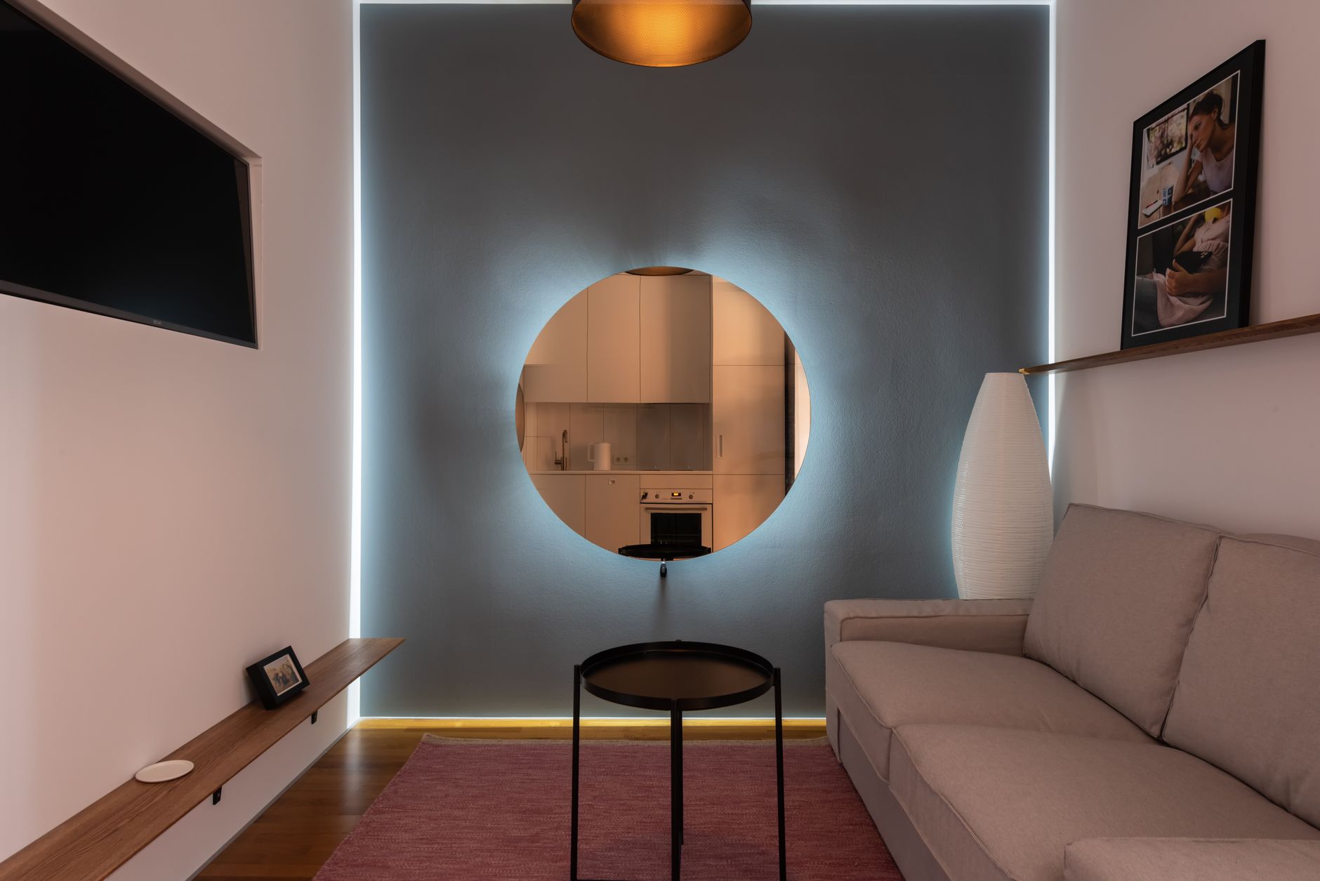 Contemporary lounge with frames and comfortable sofa in front of TV set near luminous wall with round mirror