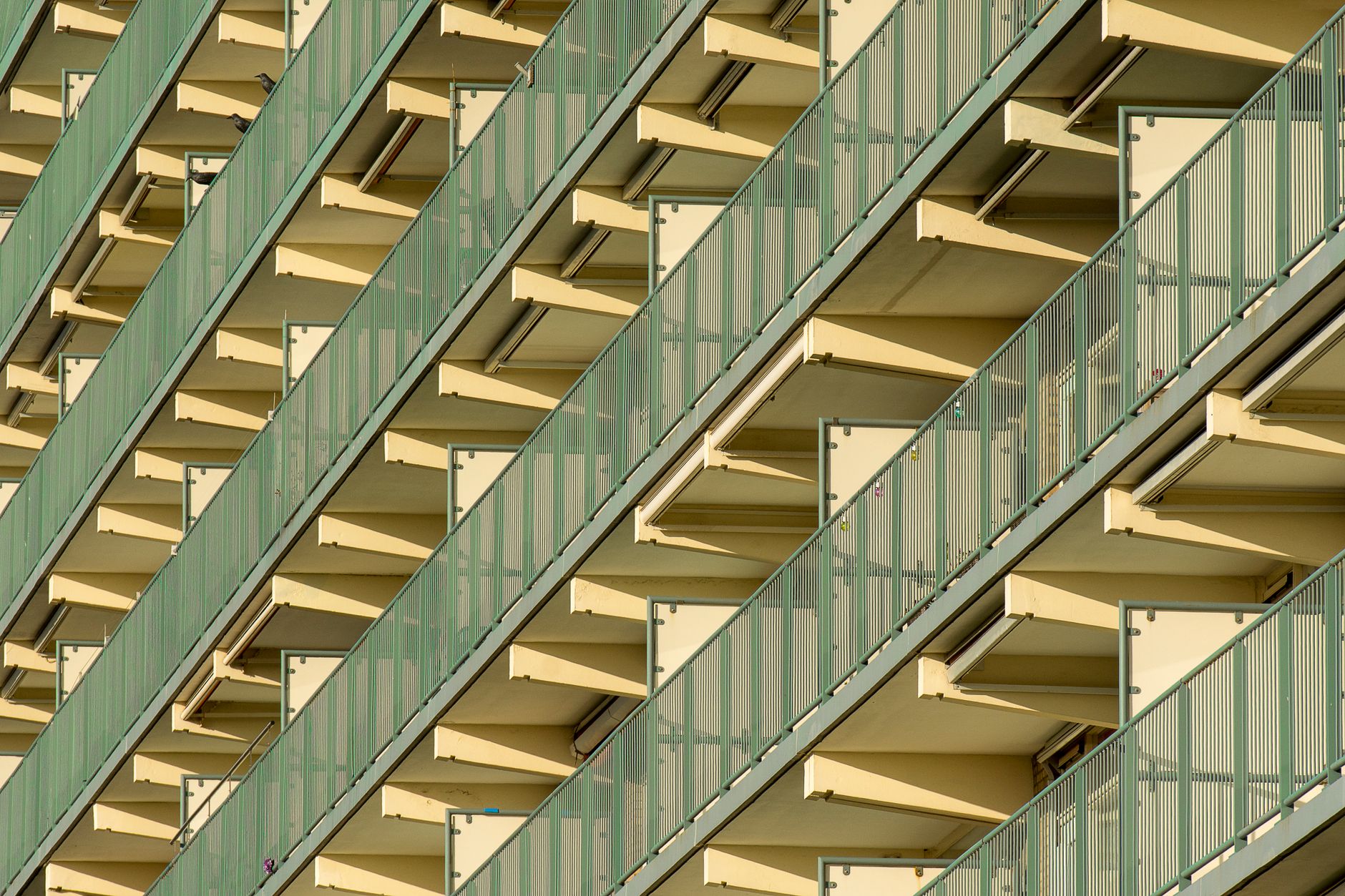 Diagonal view of a modern residential building facade with green balconies and geometric patterns.