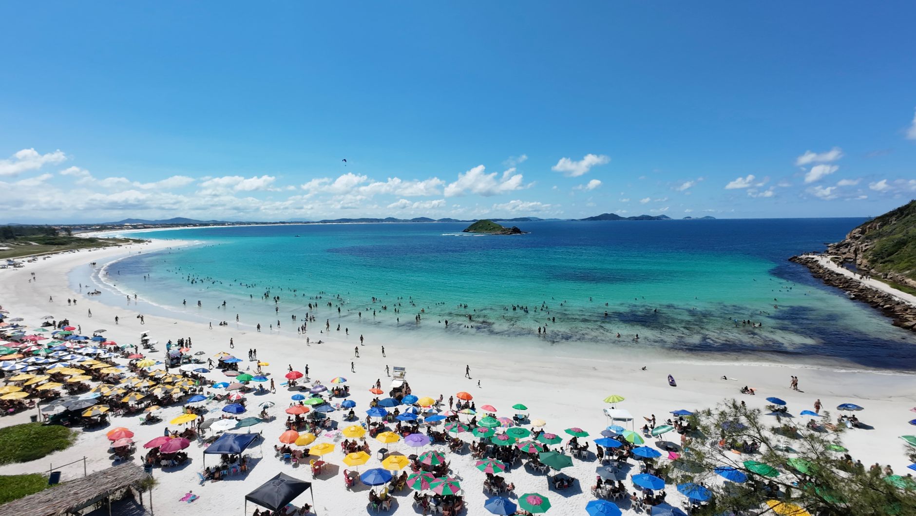 Aerial view of a lively beach with colorful umbrellas and people enjoying the sun in Arraial do Cabo, Brazil.