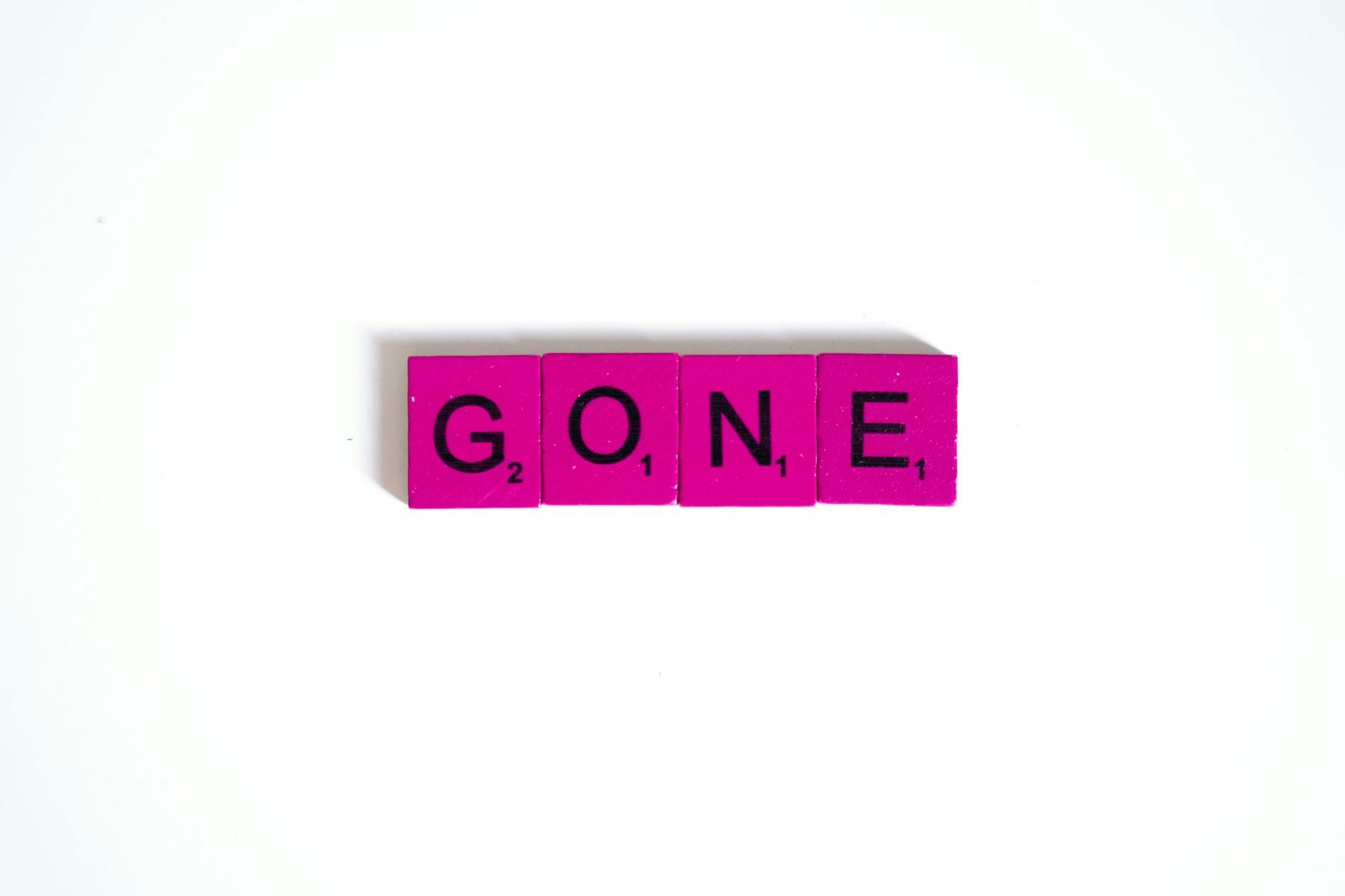 Pink scrabble tiles spelling 'gone' against a clean white background, symbolizing absence.