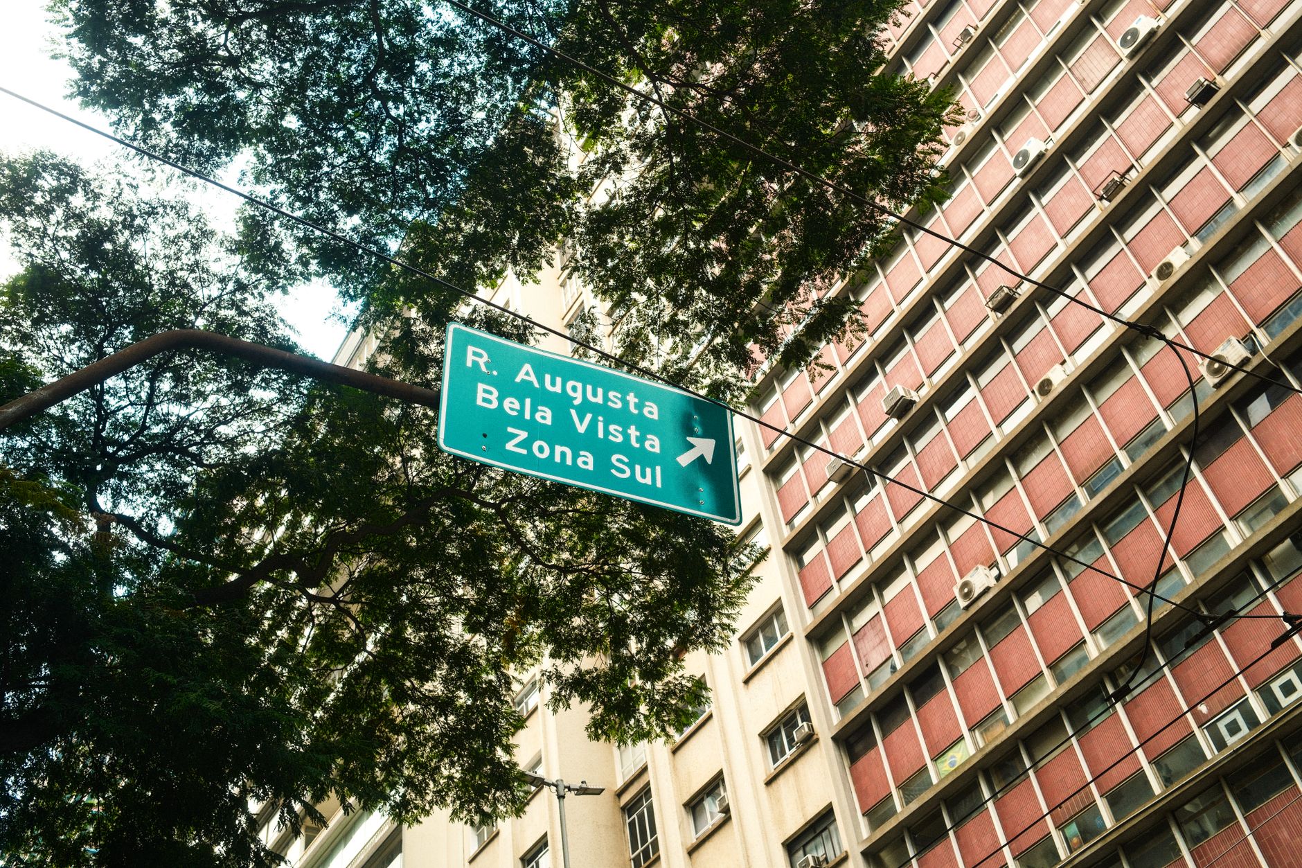 Street sign pointing to R. Augusta, Bela Vista, Zona Sul in São Paulo with urban backdrop.